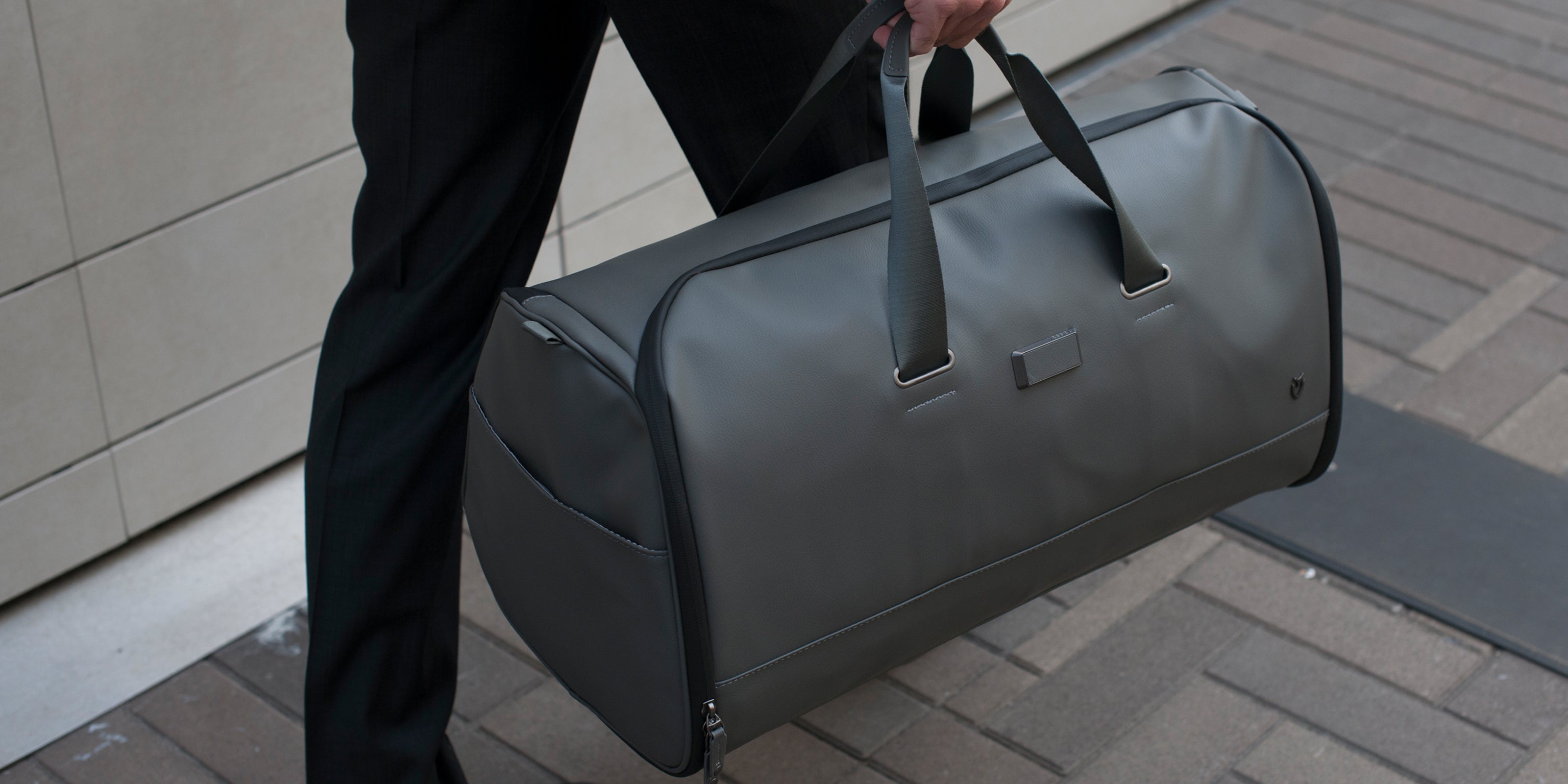 Close up of man carrying gray leather duffel bag