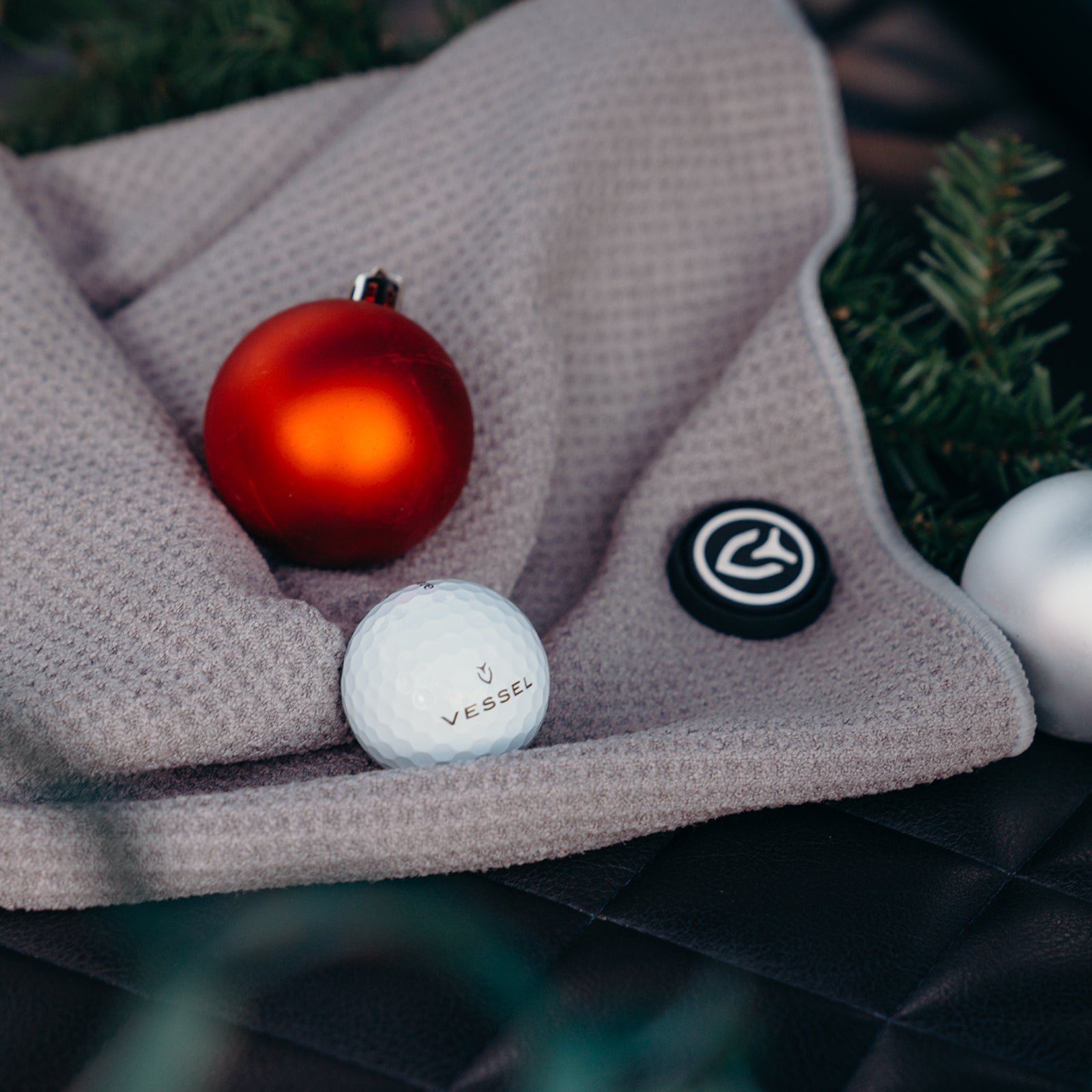Red Christmas ornament, golf ball sitting on top of VESSEL magnetic golf towel