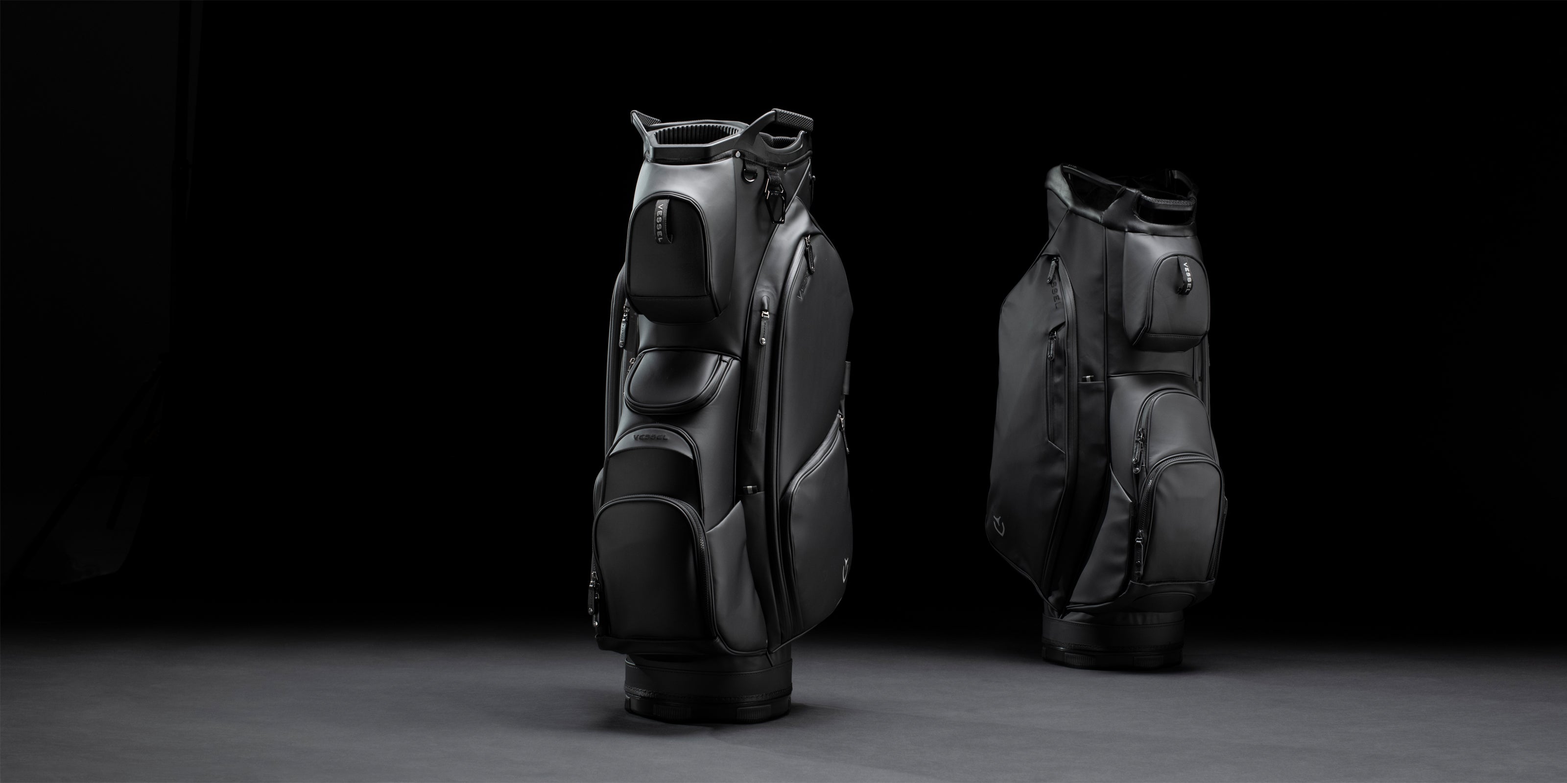 Two black golf cart bags propped upright in black studio