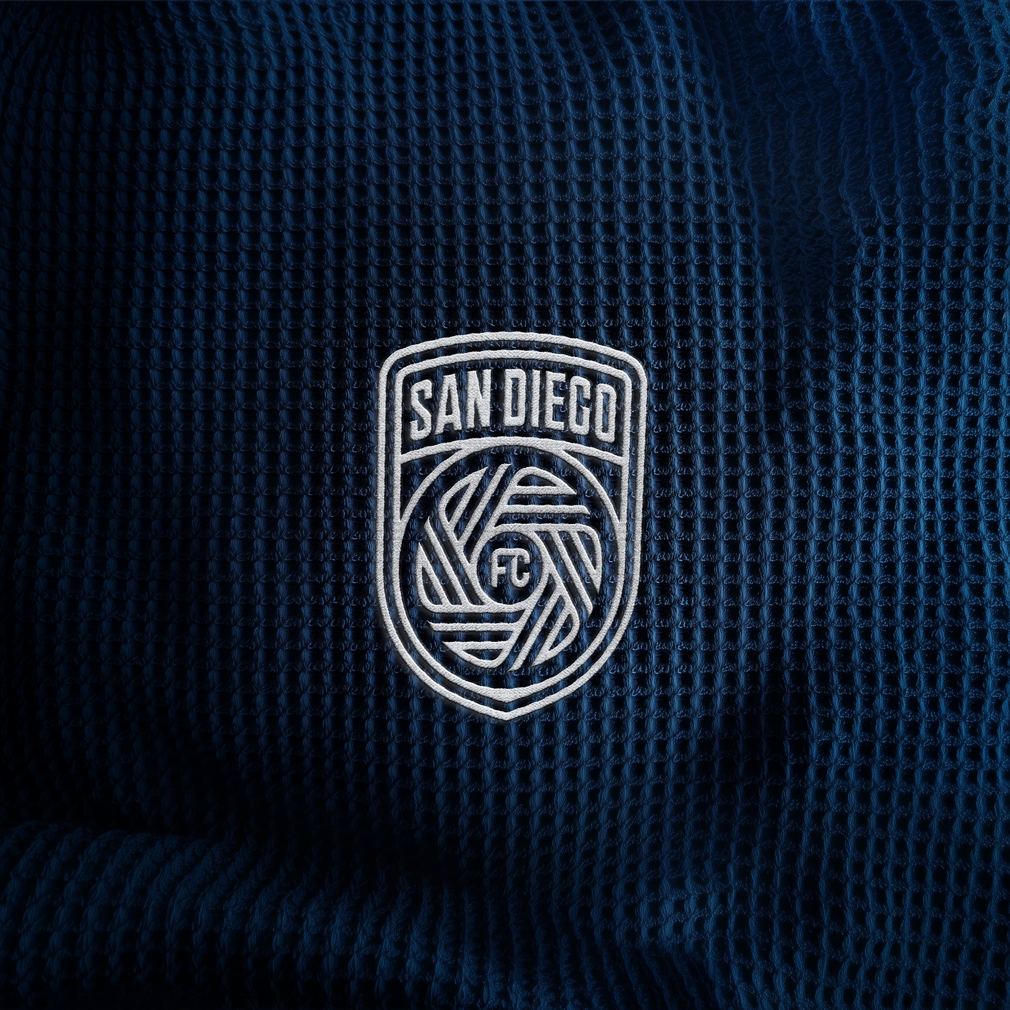Close-up of a textured dark blue fabric with 'San Diego FC' logo embroidered on it #size_20" x 20"