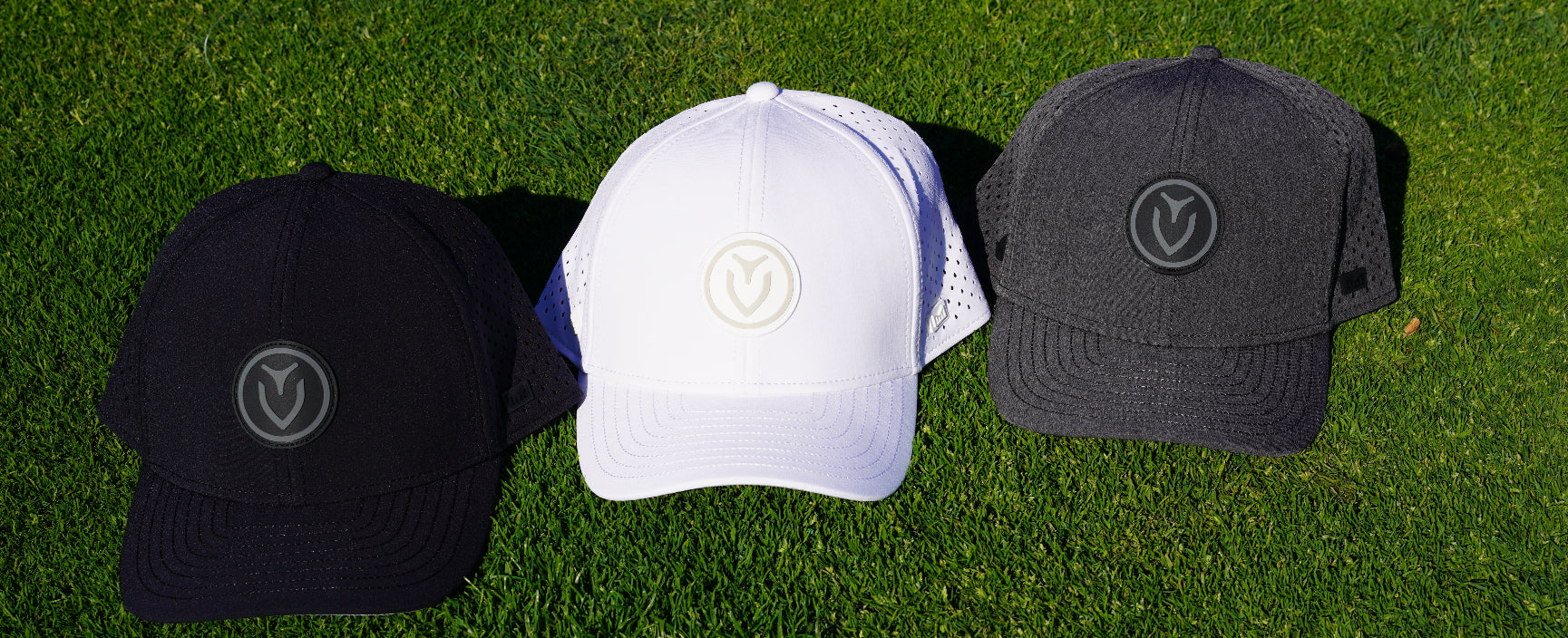Three hats in different colors, black, white, and gray, next to each other on the grass