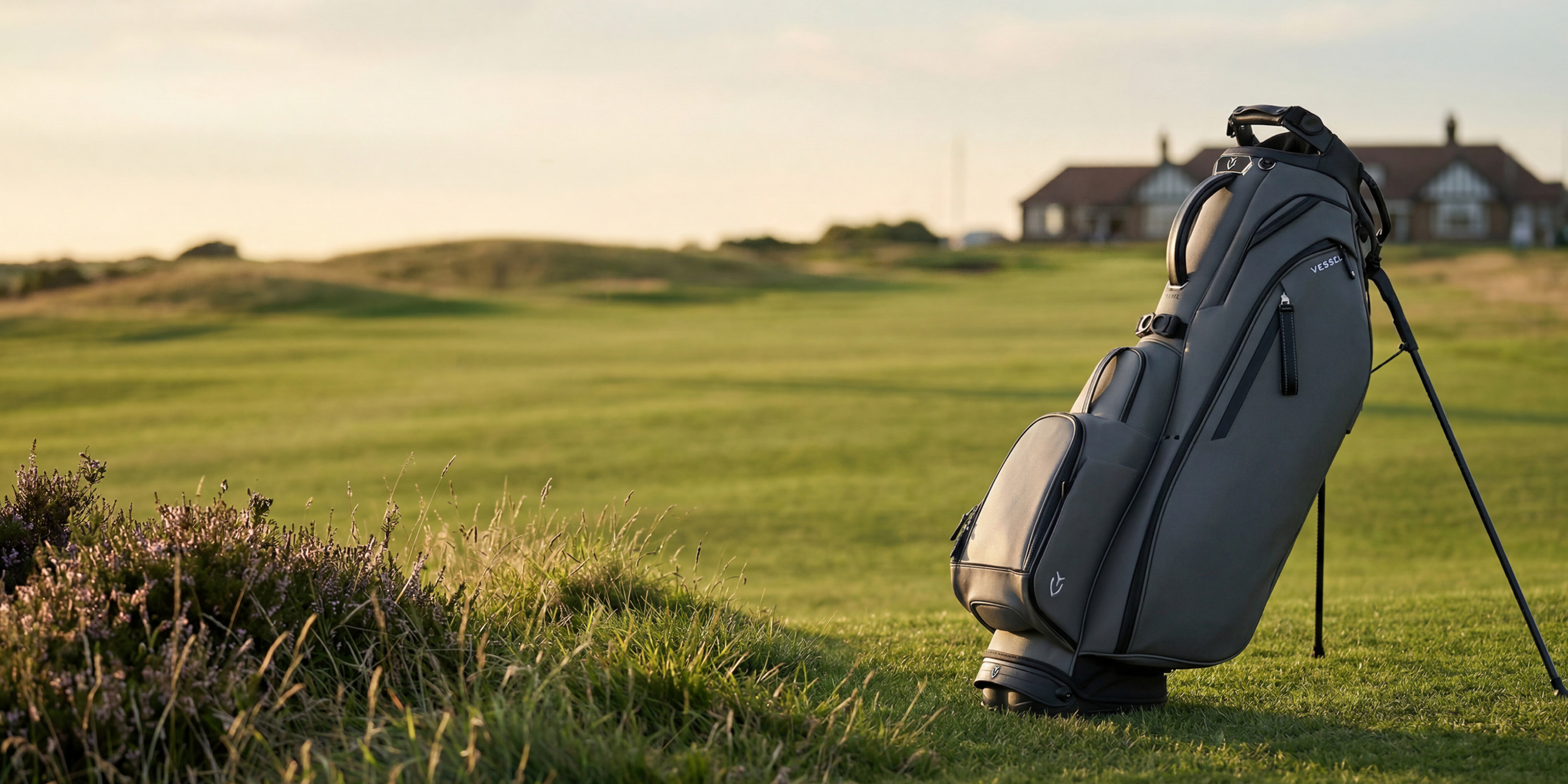Grey leather golf bag on a green golf course with house in background