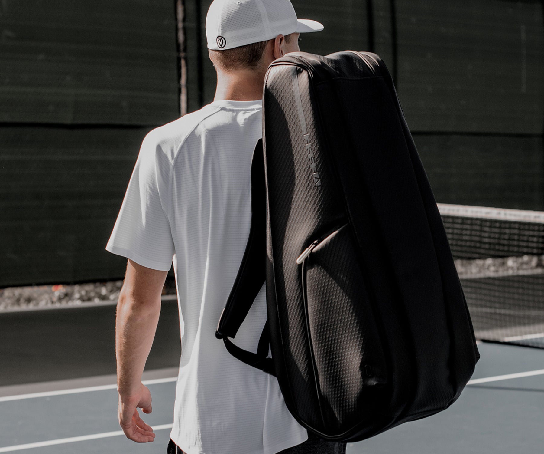 Back of tennis player on tennis court with black tennis racquet bag