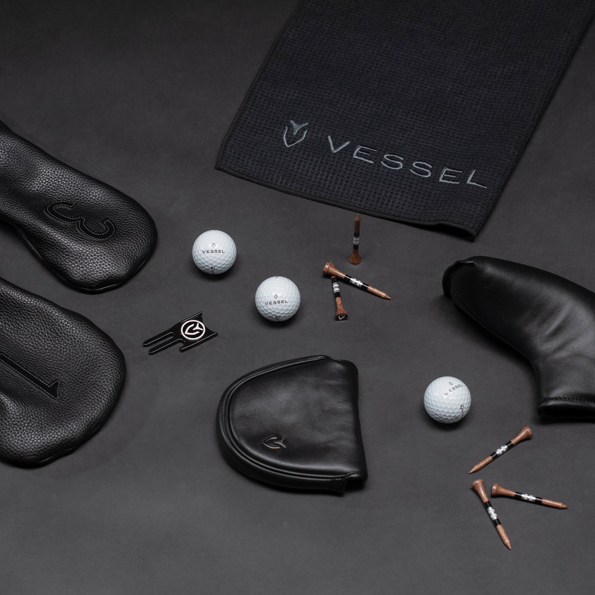 Black golf balls, golf tees, black golf headcovers, and black golf towel scattered on black background
