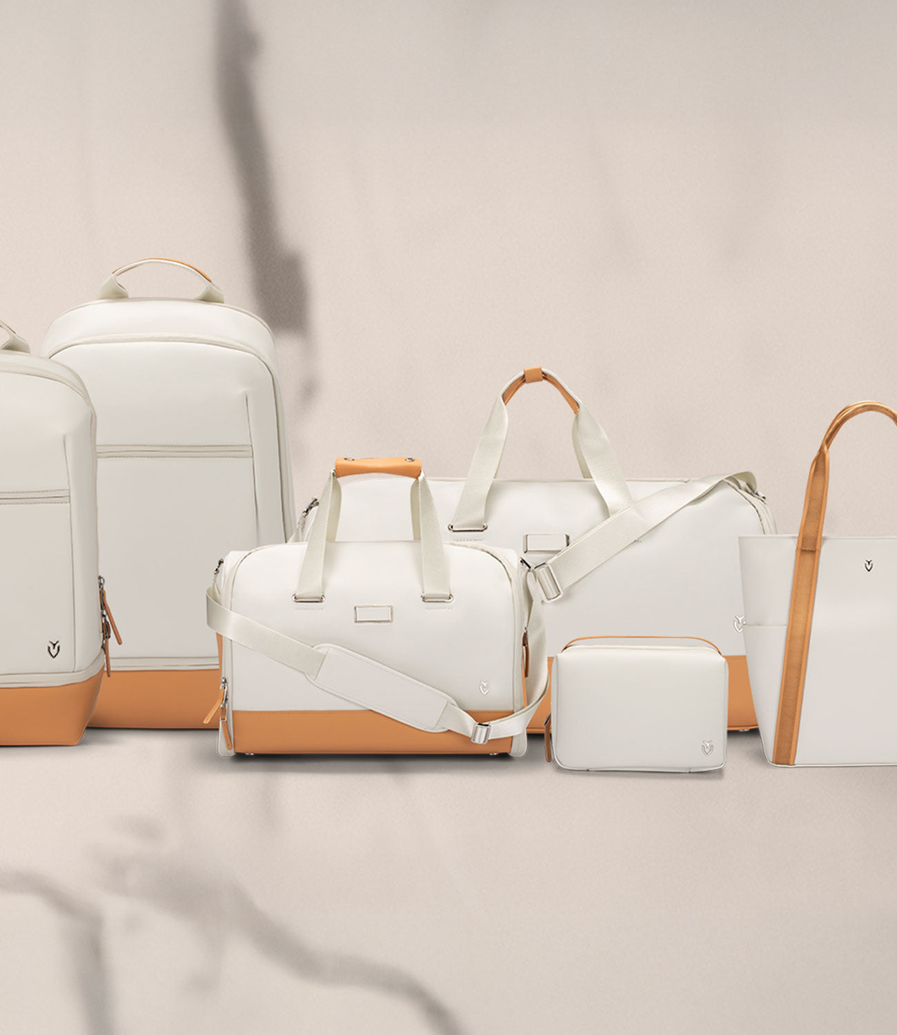 6 white and latte bags next to each other: Signature Backpack, Signature Plus Backpack, Signature Weekender, Signature Garment Duffel, Lux Toiletry, Signature Tote