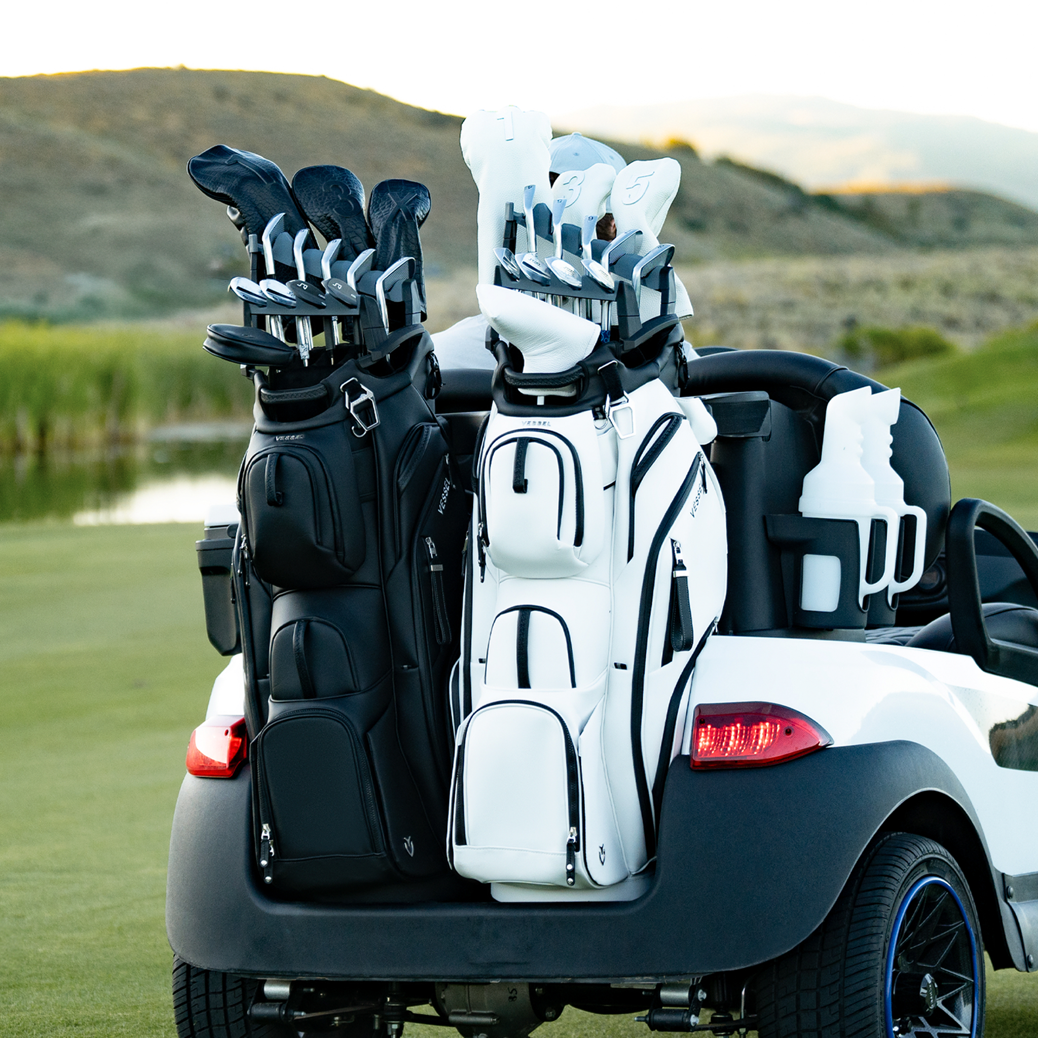 One black, one white Lux Pro Cart II bags on back of golf cart on a green golf course