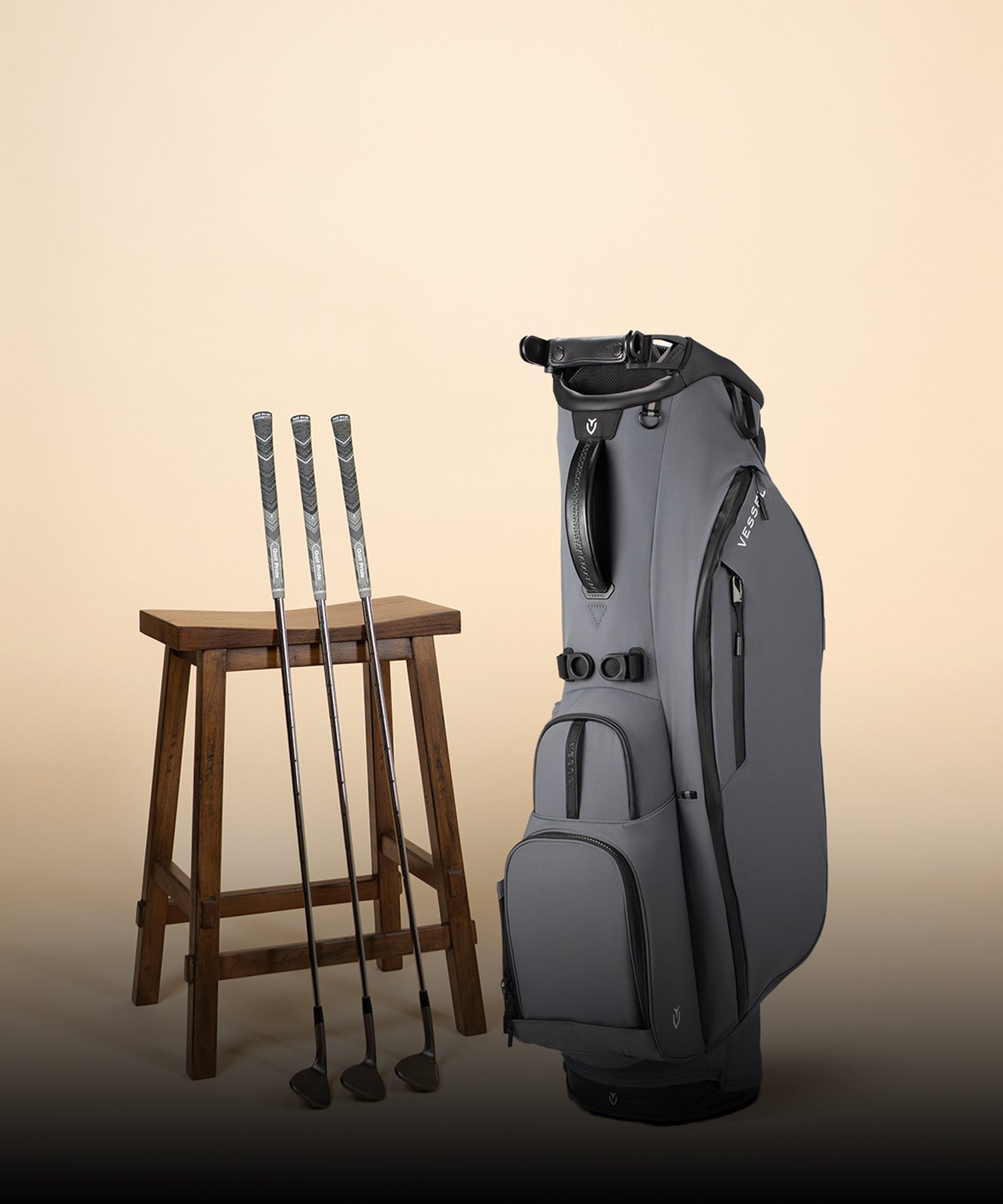 Grey Player Air stand bag next to three golf clubs and a wooden stool