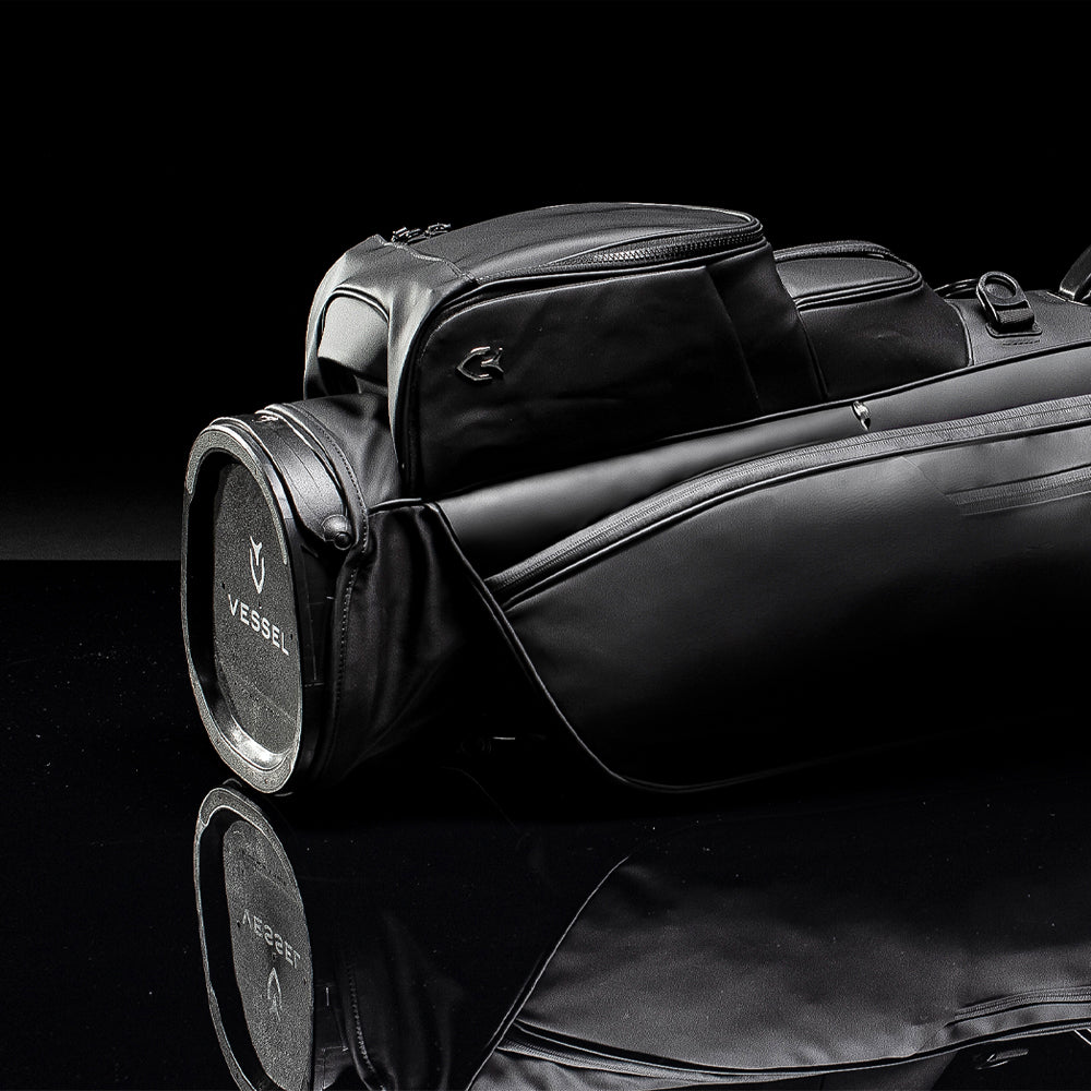 Black golf stand bag laying on ground with black background and reflection