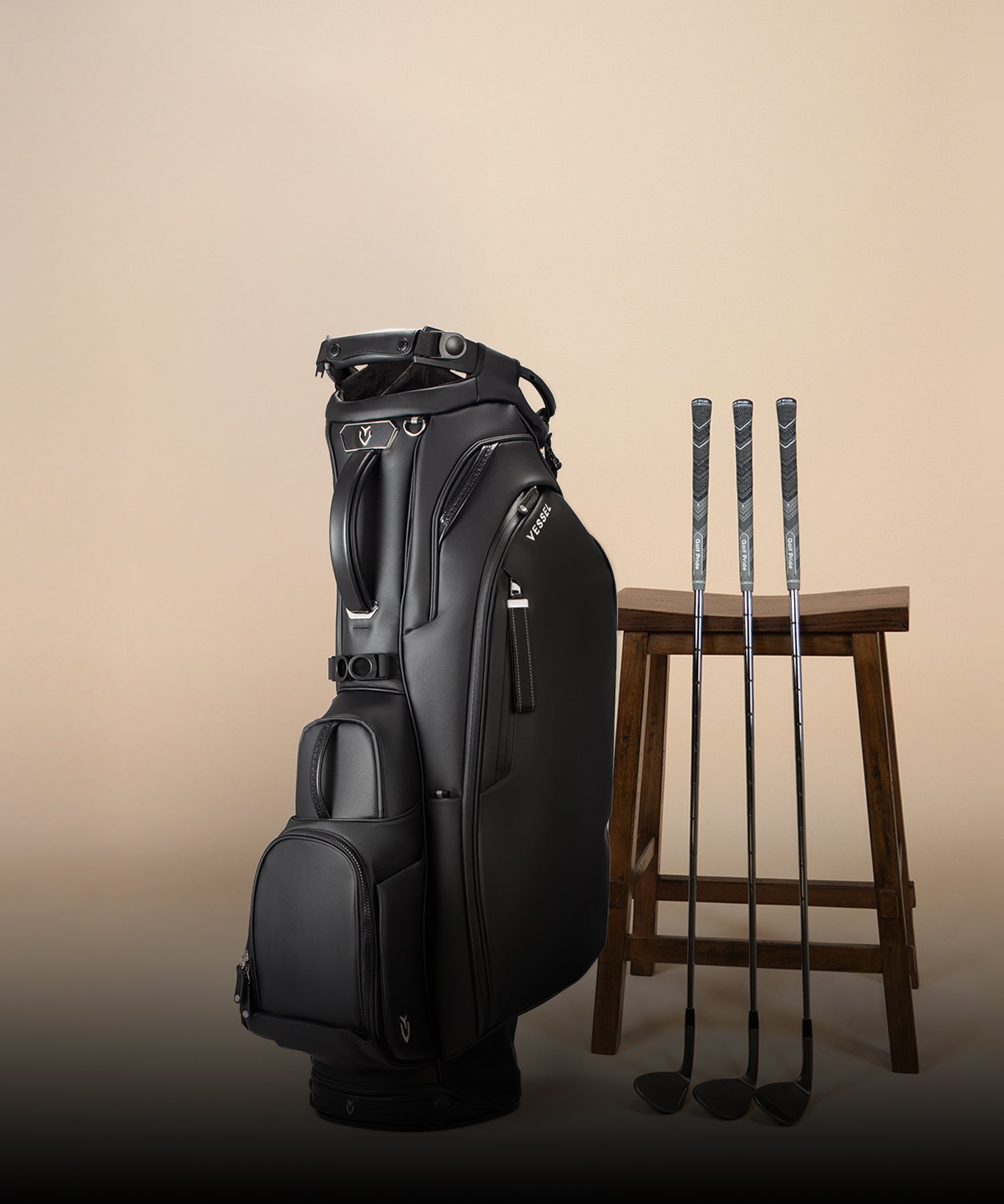 Black Player V Pro stand bag next to three golf clubs and a wooden stool