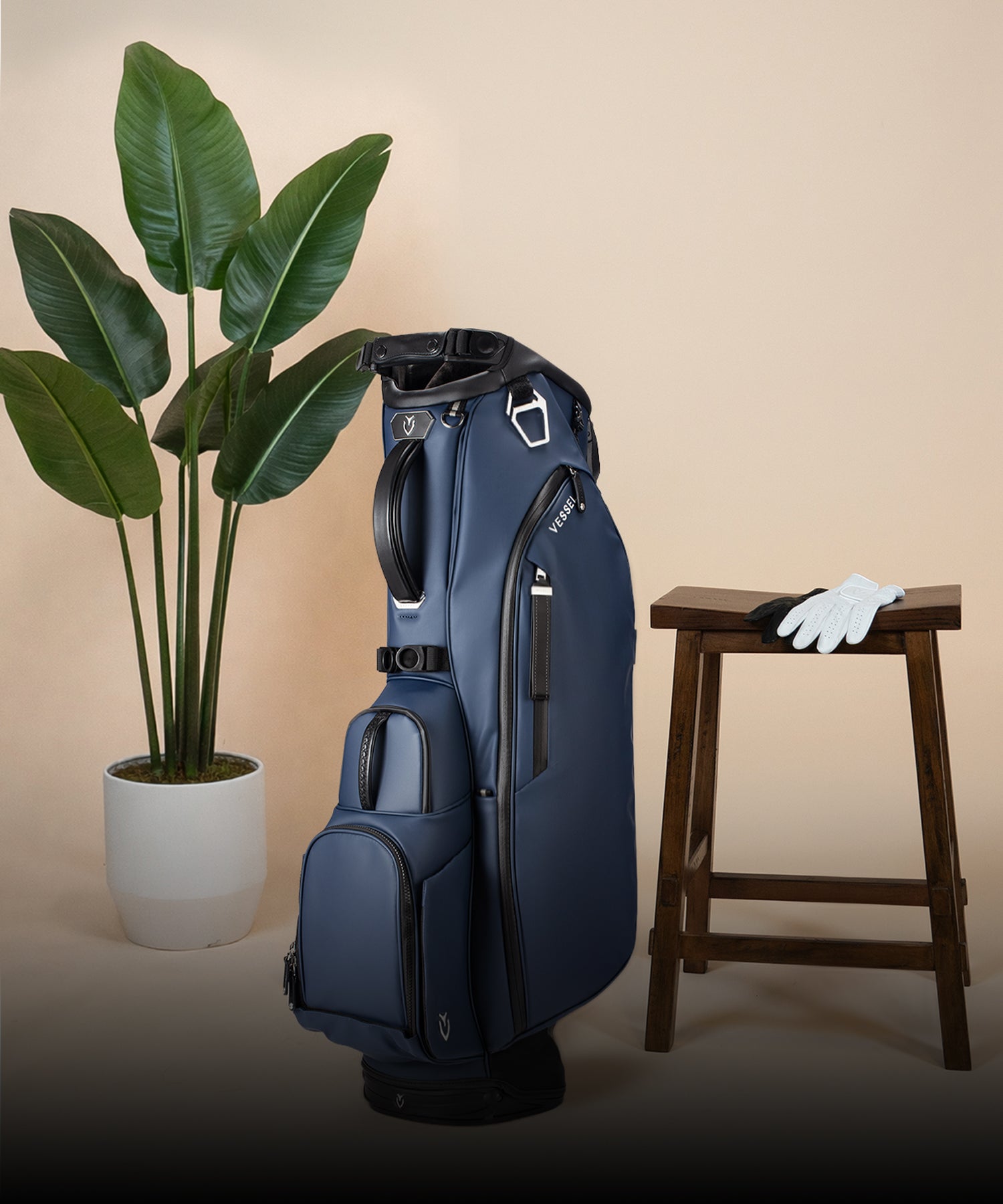Navy Player V stand bag next to three golf clubs and a potted plant