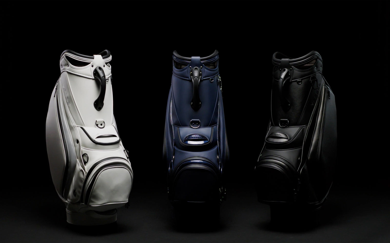 White staff bag, navy staff bag and black staff back in a row in a black studio