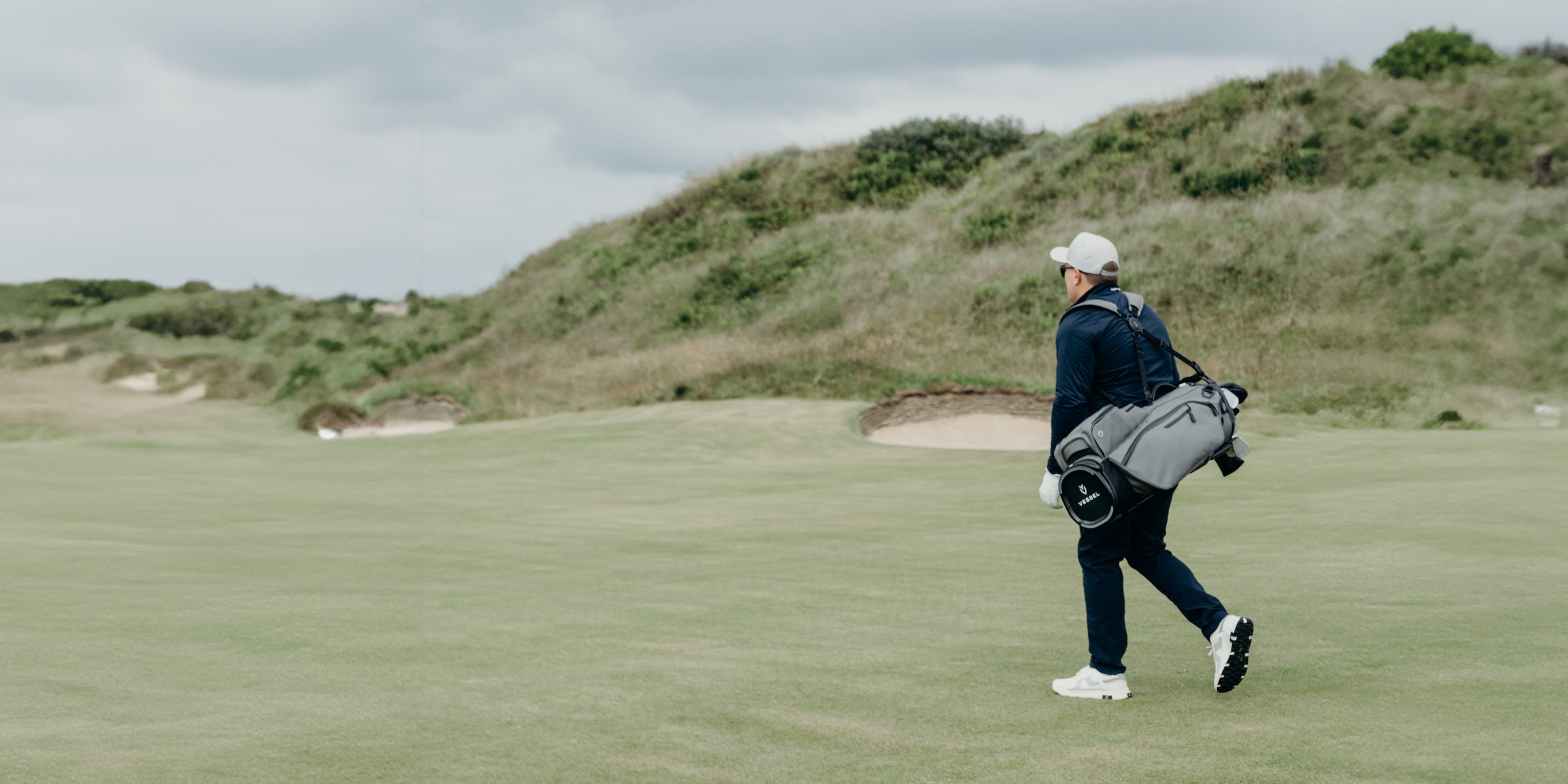Golfer carrying a grey golf stand bag on a golf course