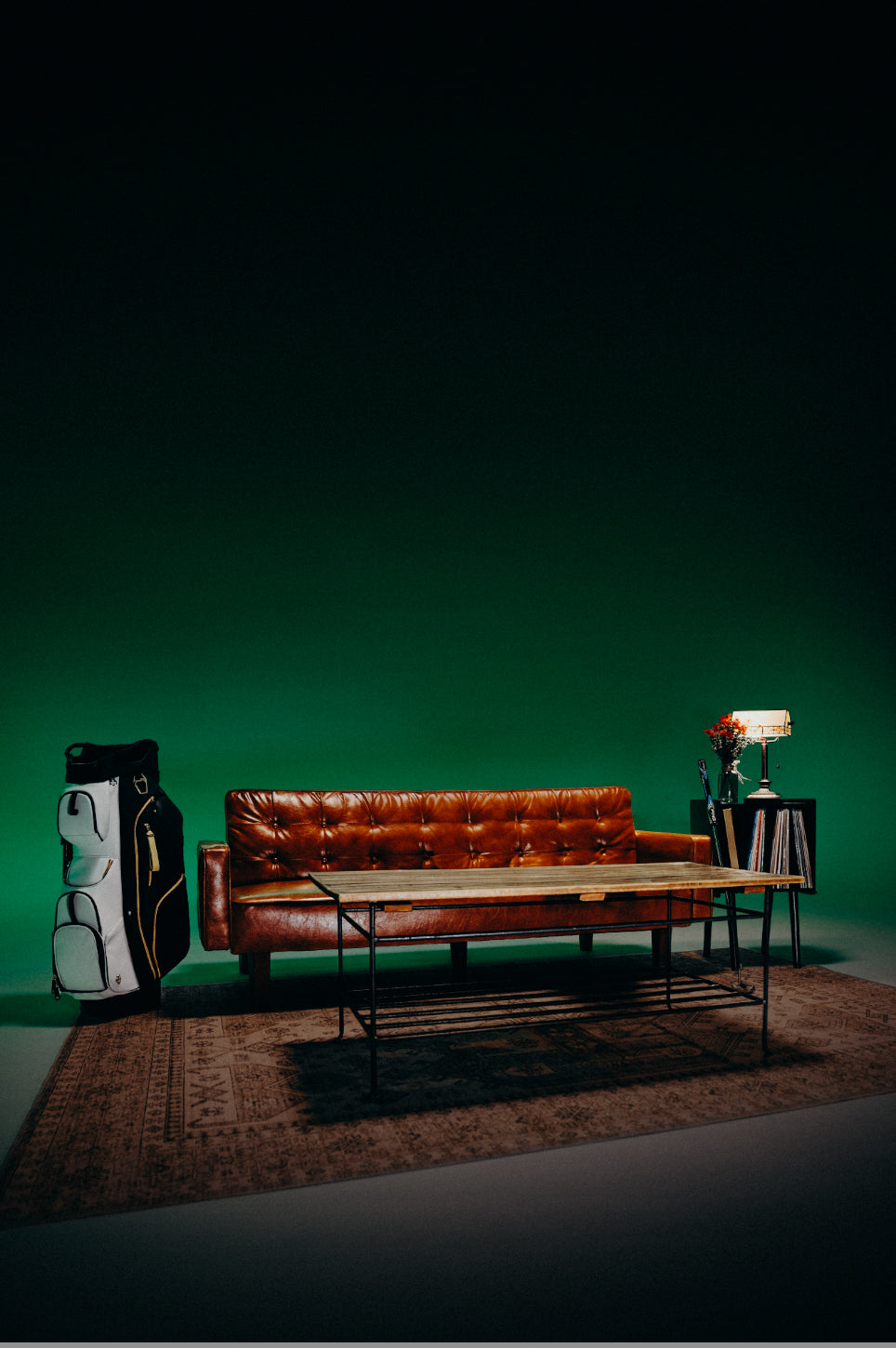 A brown couch with a wooden table in front of it. A vase of red azalea flowers are to the right and a 2025 Season Opener Lux Pro Cart is to the left of the couch.