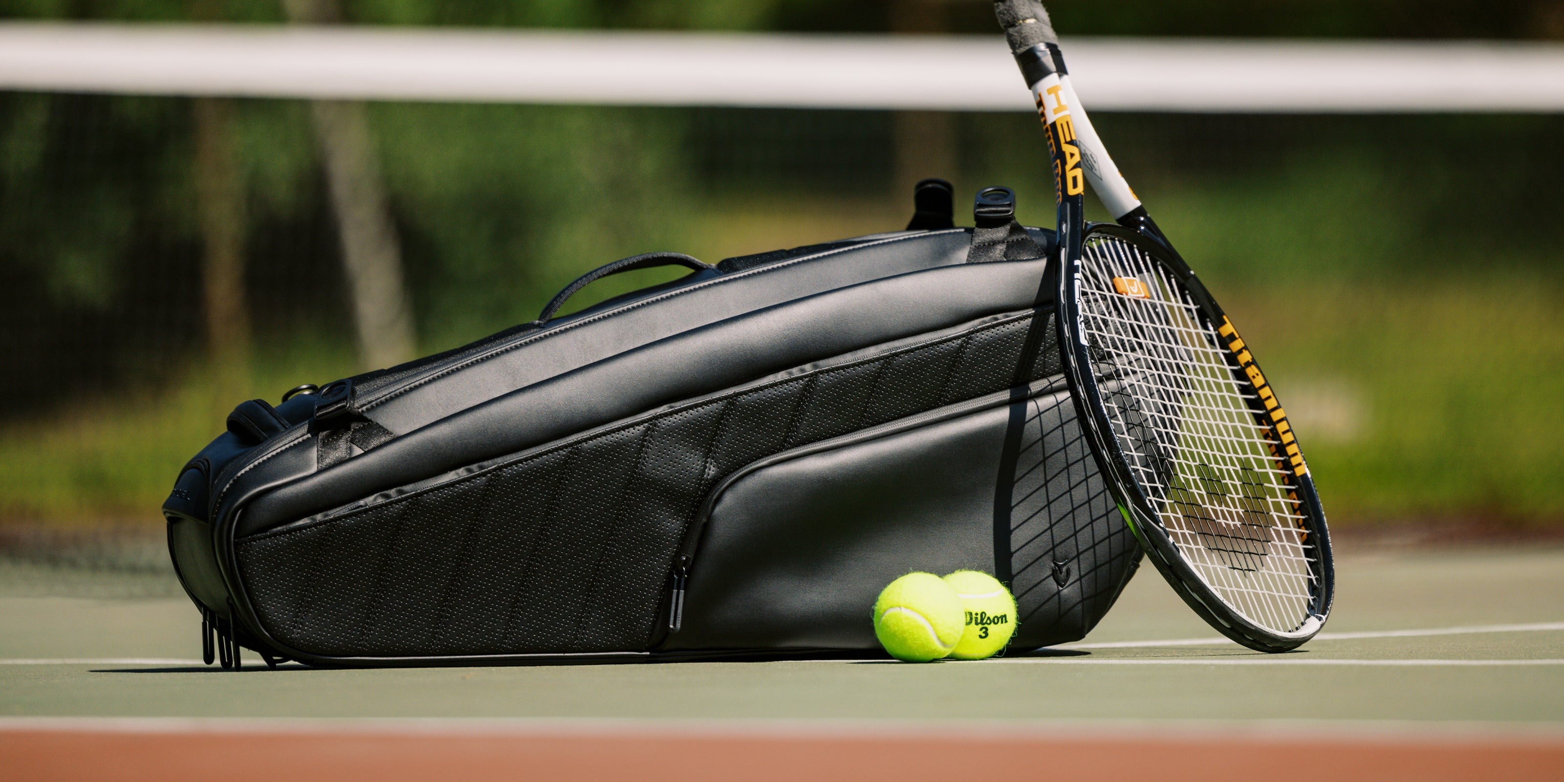 A tennis racquet resting on a a black baseline 2.0 racquet bag.