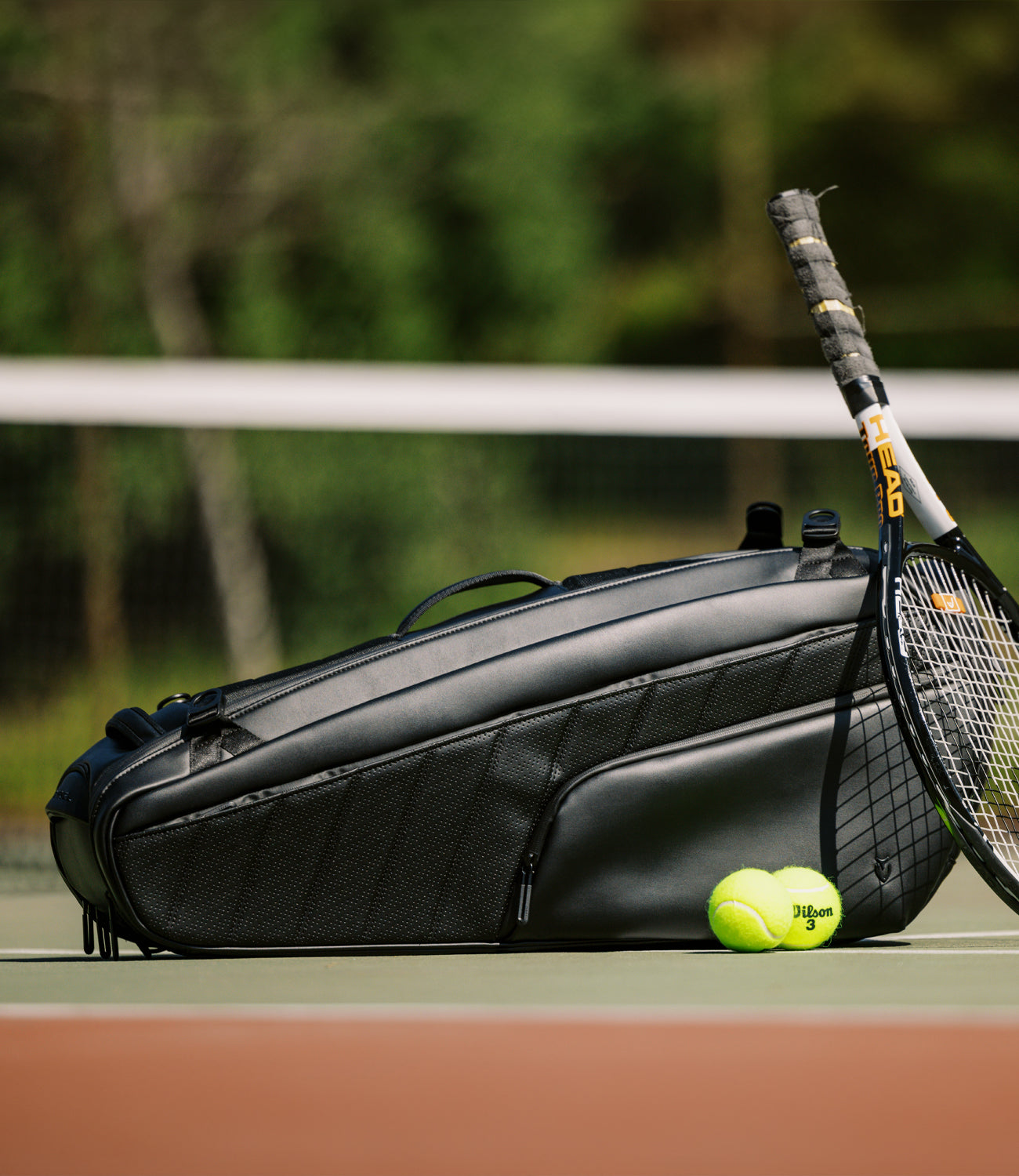 A tennis racquet resting on a a black baseline 2.0 racquet bag.