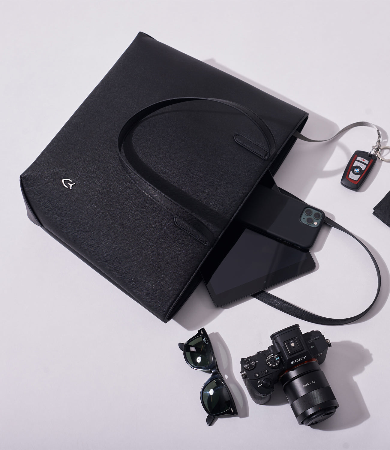 Lay flat with black leather tote with black phone, black tablet, black glasses, car keys, and camera