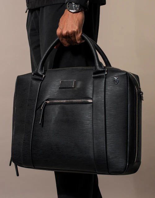 Model wearing all black holds a black Signature Briefcase in a brown studio