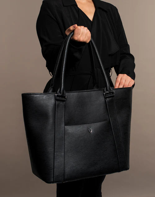 Model wearing black holds a black leather Signature Laptop Tote in a brown studio
