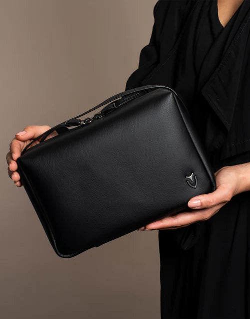 Model wearing black holds a black Signature Toiletry bag in a brown studio