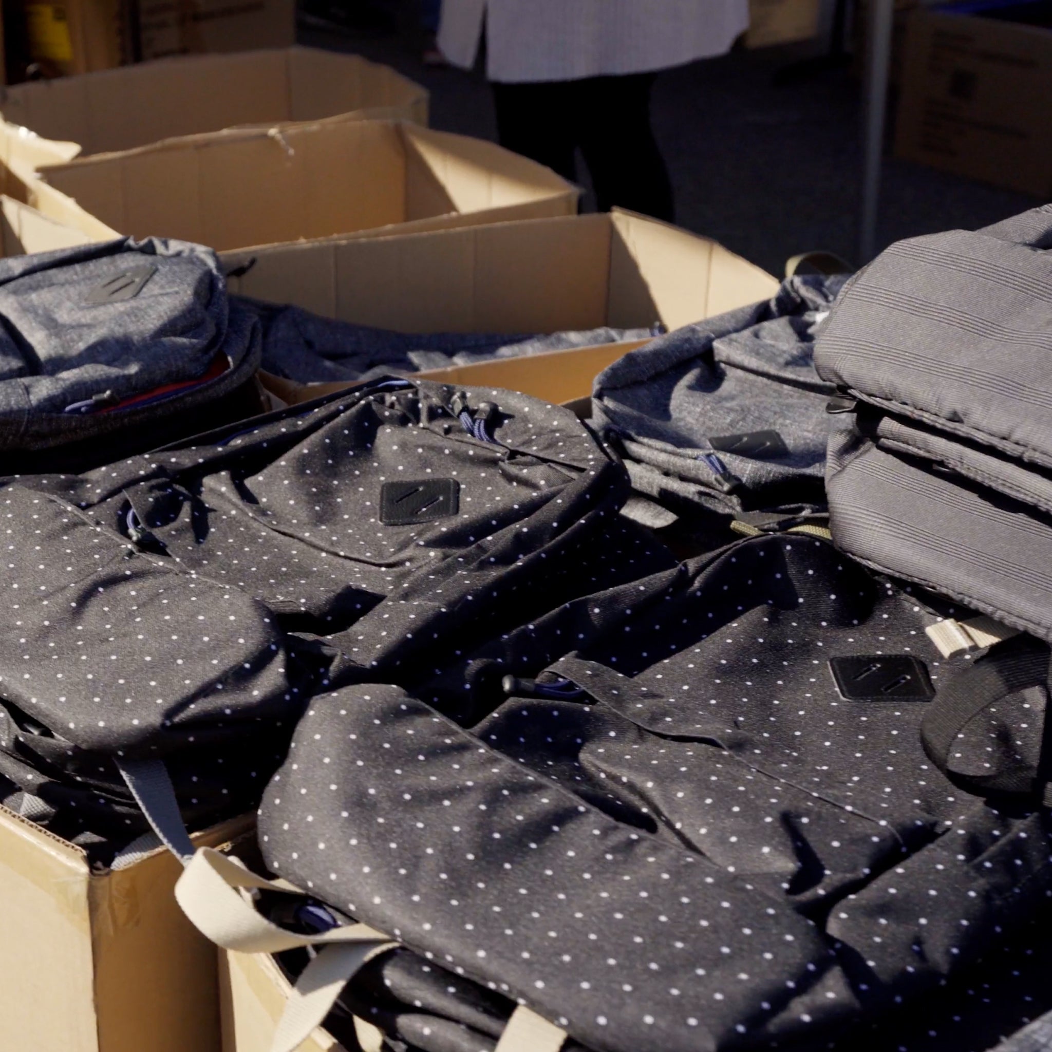 Many big cardboard boxes are filled with black spotted backpacks