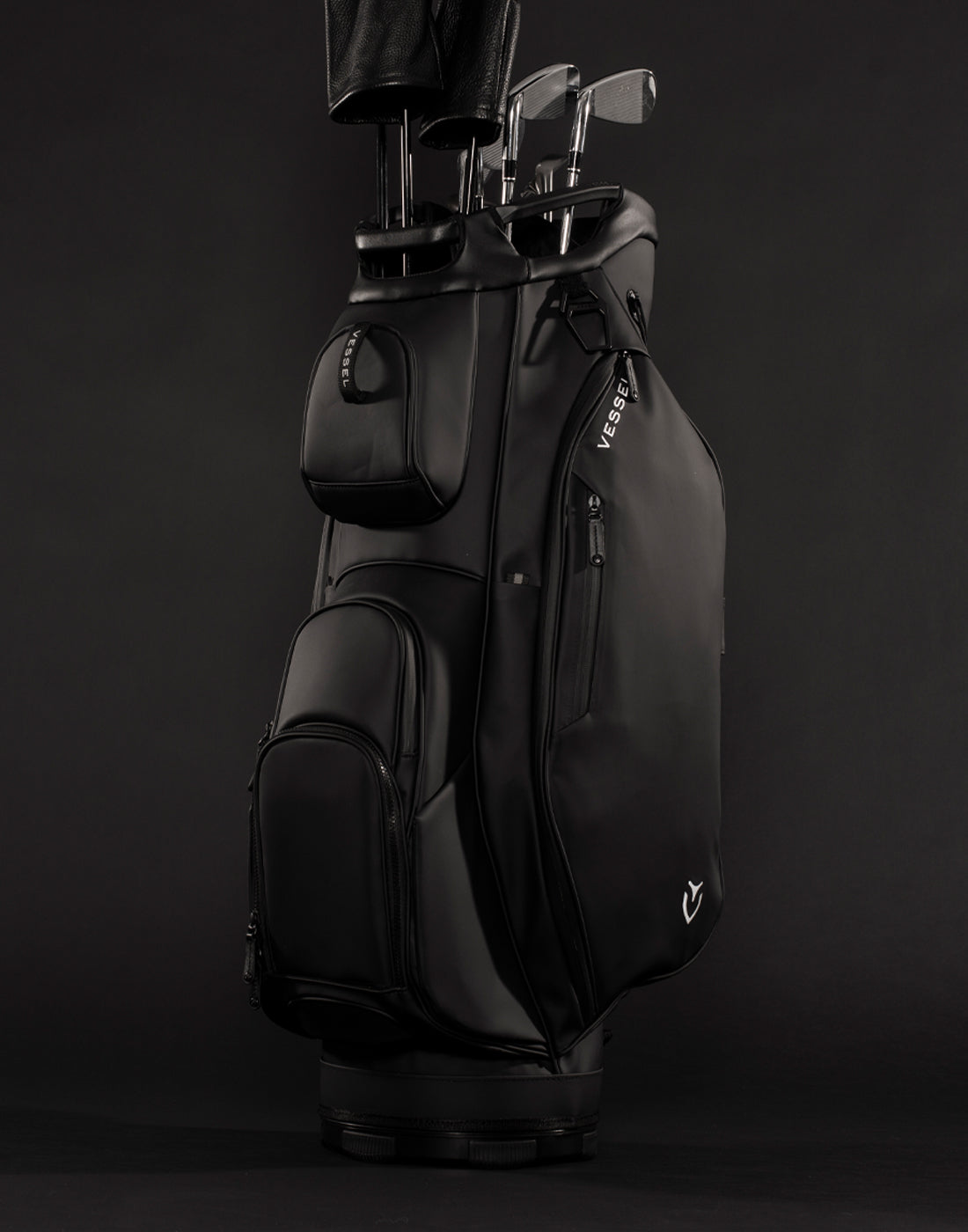 Black golf cart bag filled with golf clubs propped upright in black studio