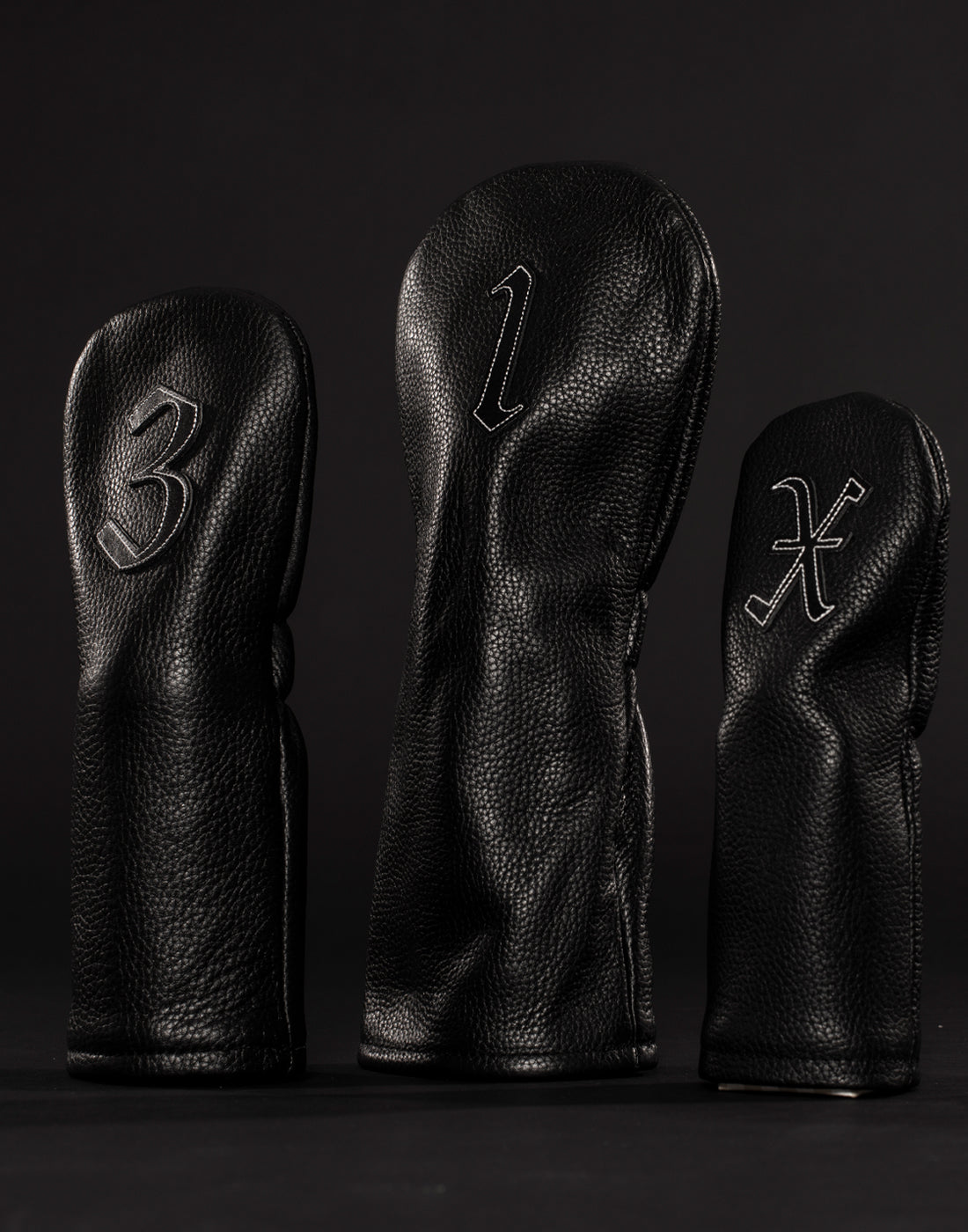 Three black golf headcovers propped upright in black studio