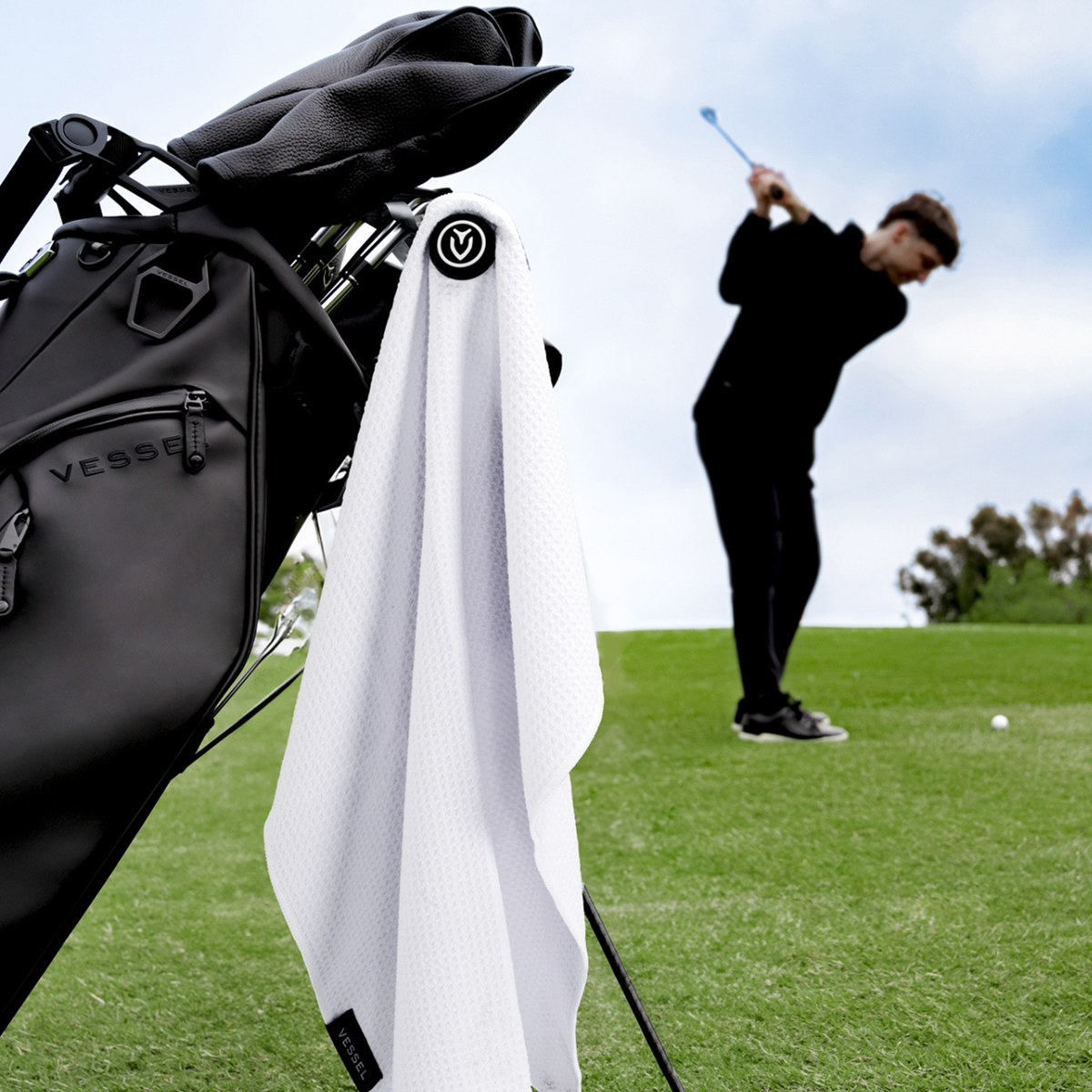 A white magnetic golf towel handing from a black golf stand bag infront of a golfer
