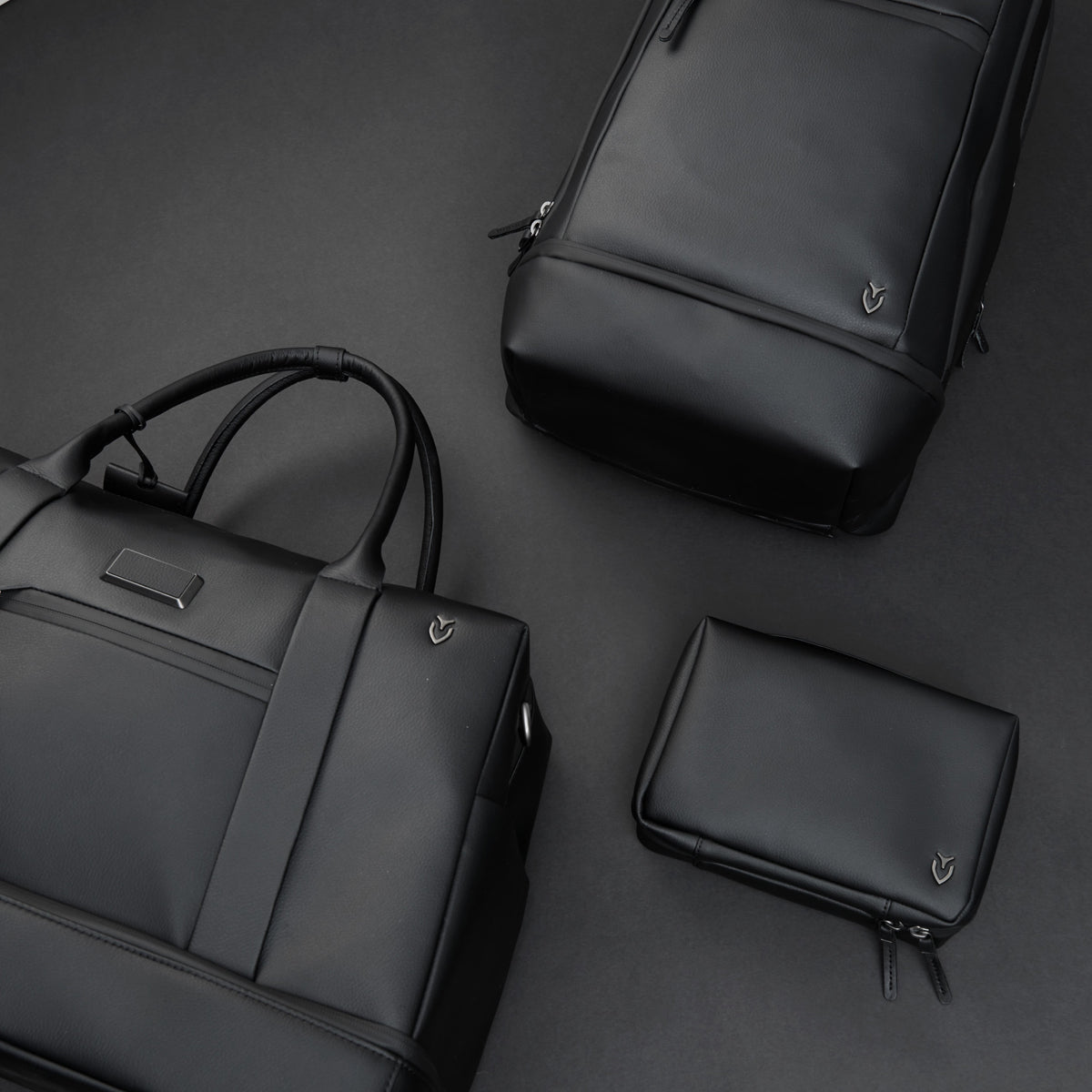 A black Signature Toiletry bag, Signature Boston duffel, and Signature Plus Backpack are placed on a black background