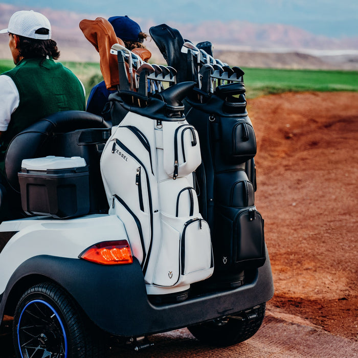 two men are driving a golf cart with cart bags on the back