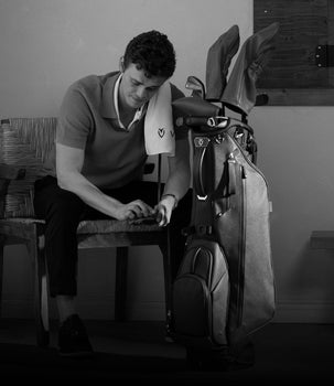 A golfer is sitting next to a golf bag with a towel over his shoulder