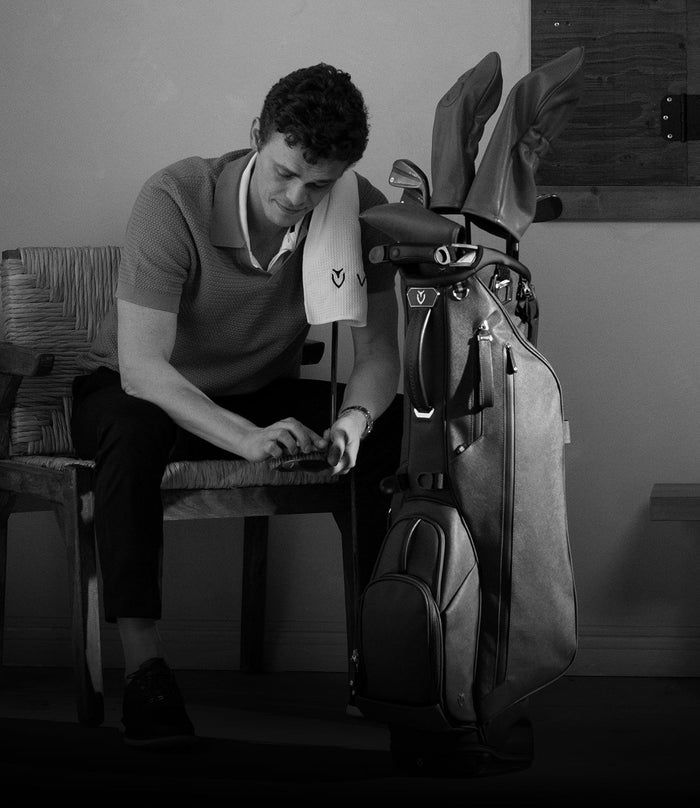 A golfer is sitting next to a golf bag with a towel over his shoulder