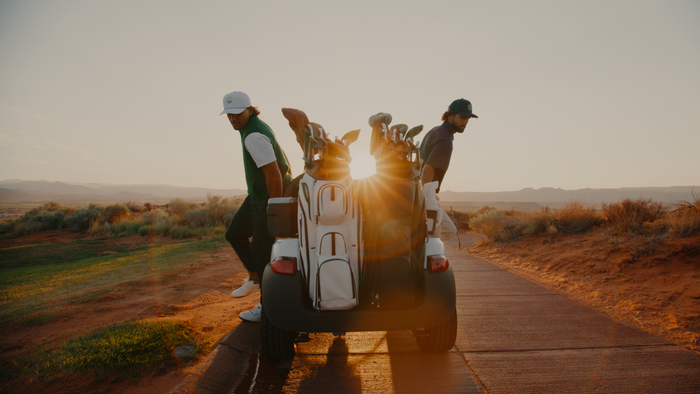 two men getting off a golf cart with two golf carts on the back at sunset