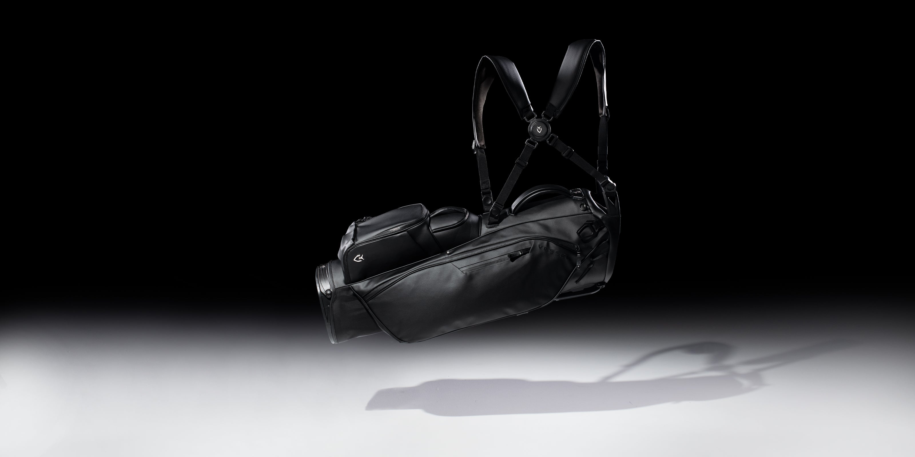 Floating black leather golf stand bag in black studio with gray flooring