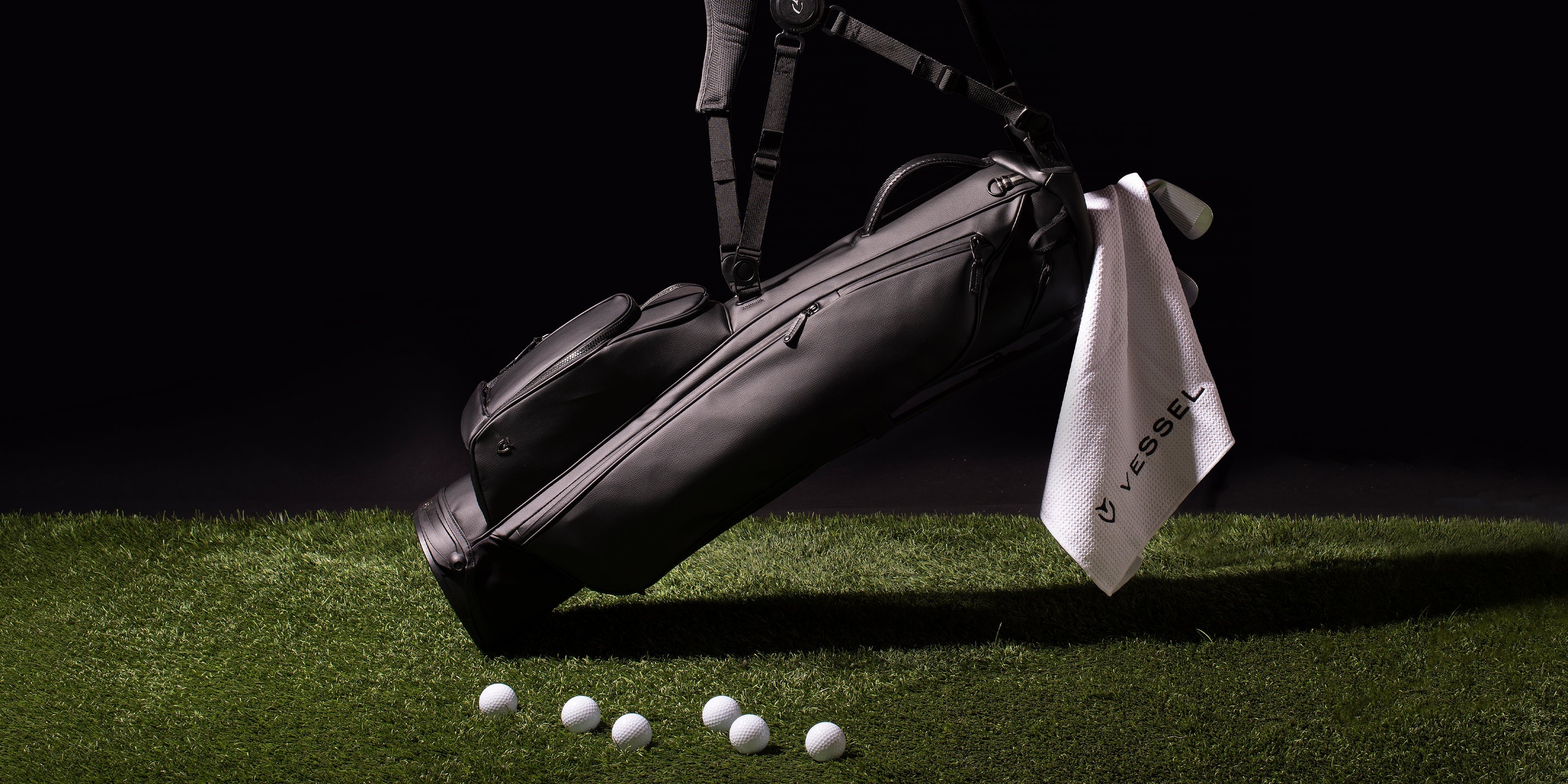 Black floating golf stand bag with hanging white towel on green grass with scattered golf balls