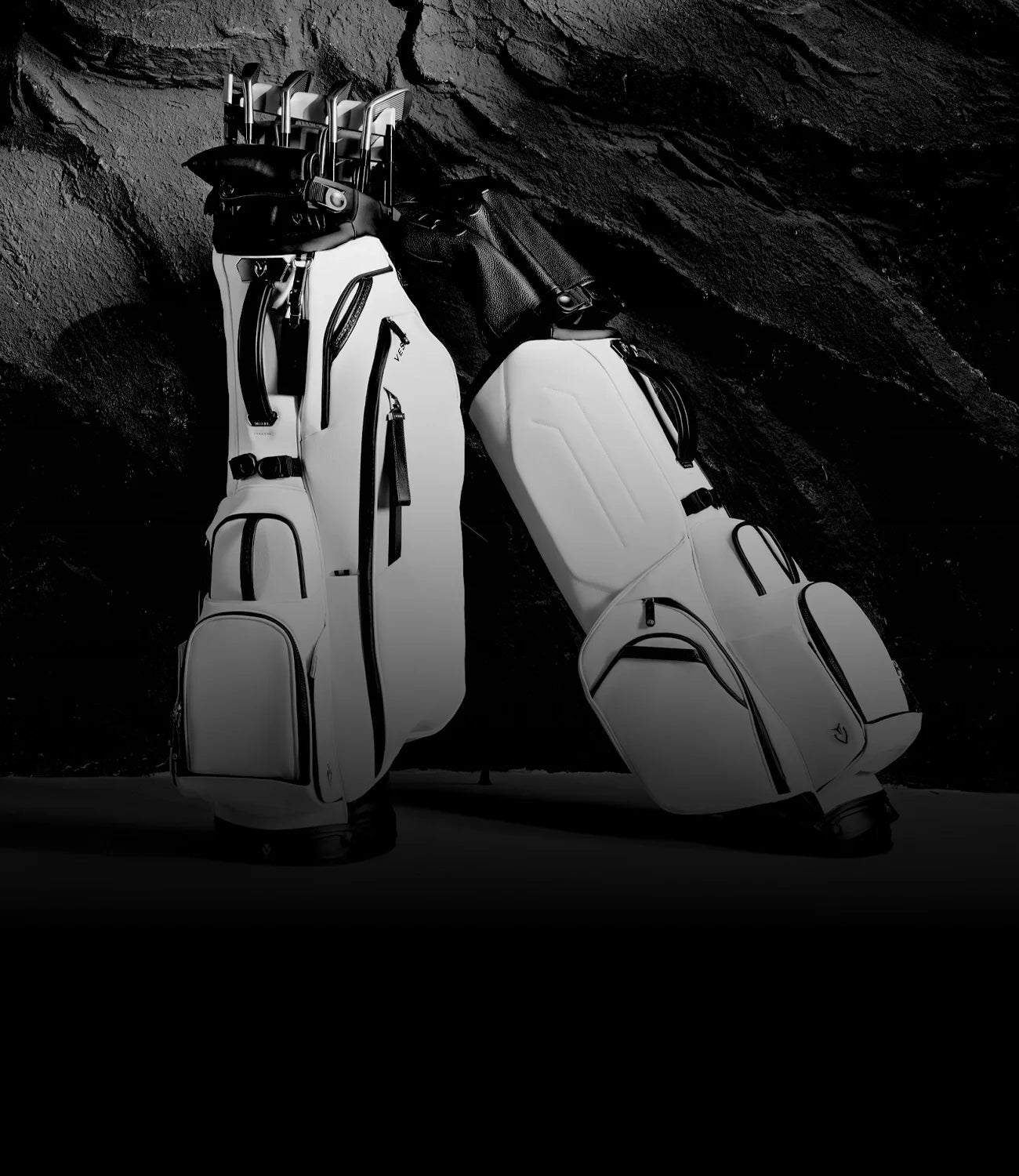 Two white leather golf stand bags against a dark, rocky wall