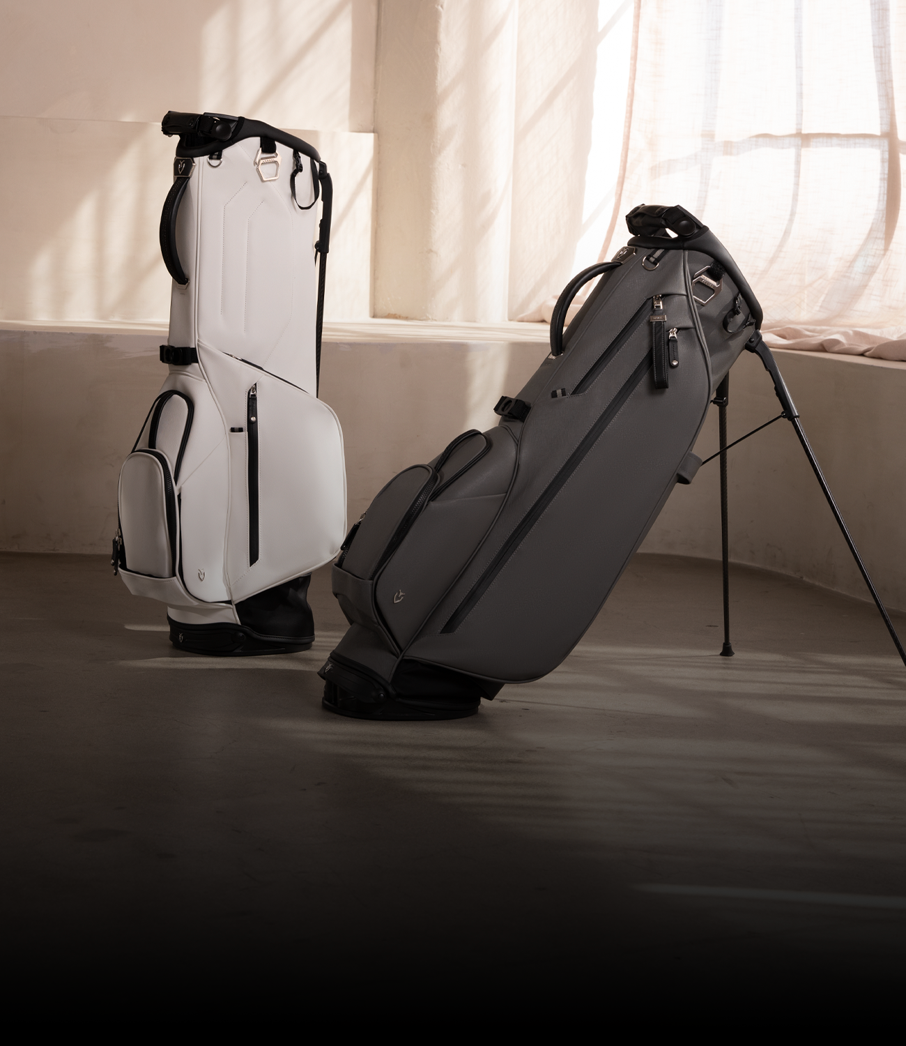A white golf bag and a grey golf bag in a concrete room