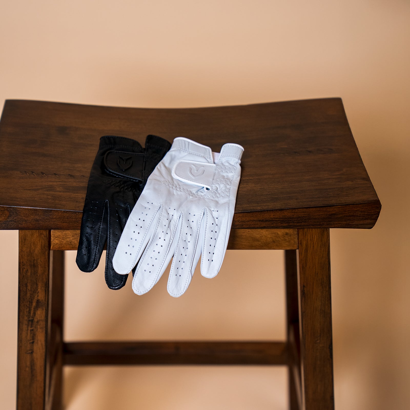 A black and a white leather golf glove sitting on wooden stool