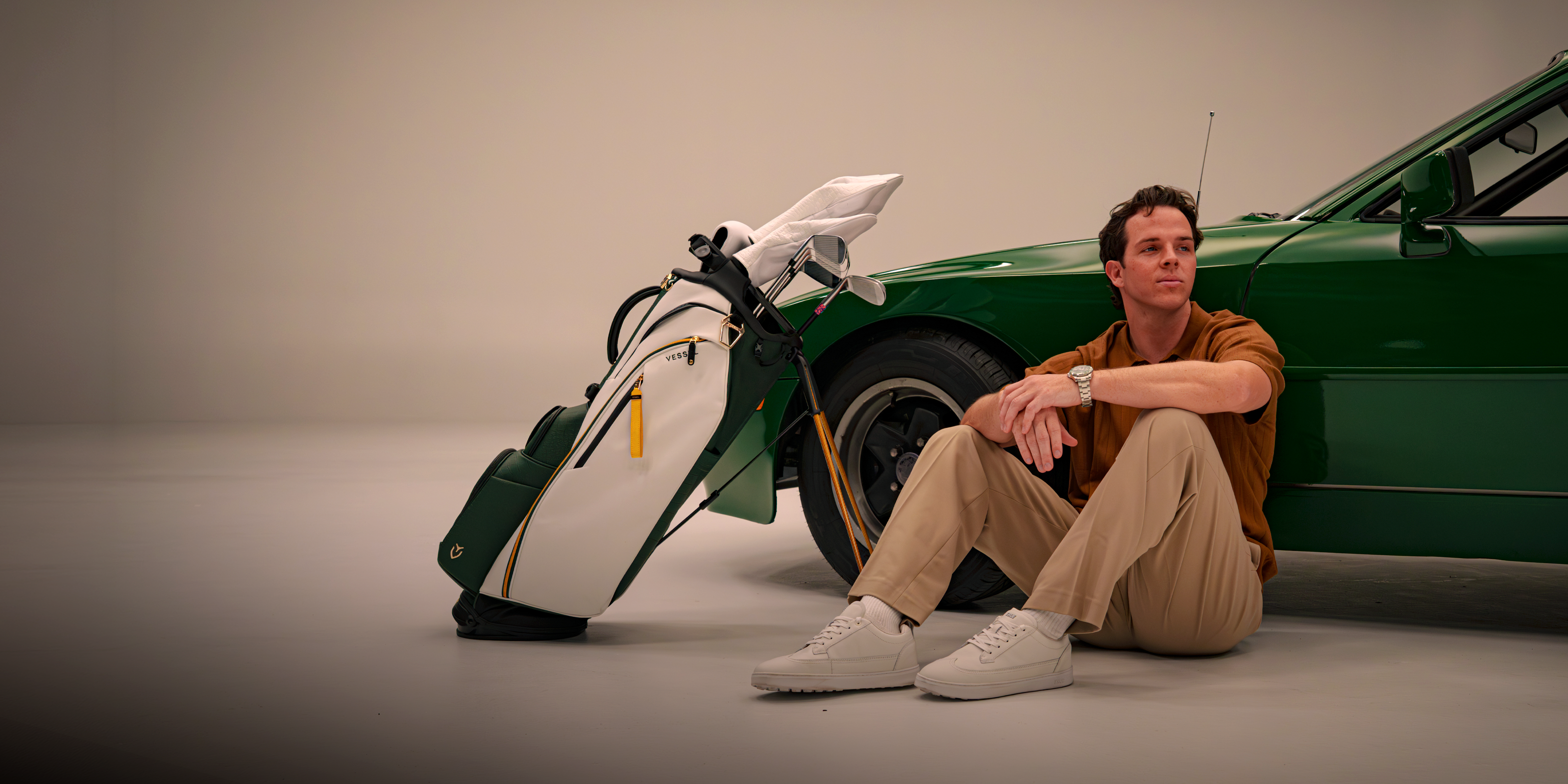 Man sitting next to Season Opener 2026 Golf bag and green porsche