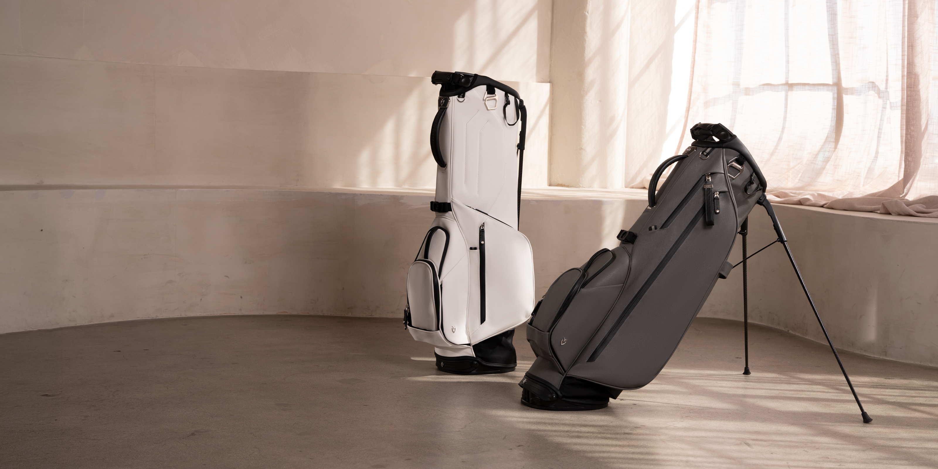 A white golf bag and a grey golf bag in a concrete room