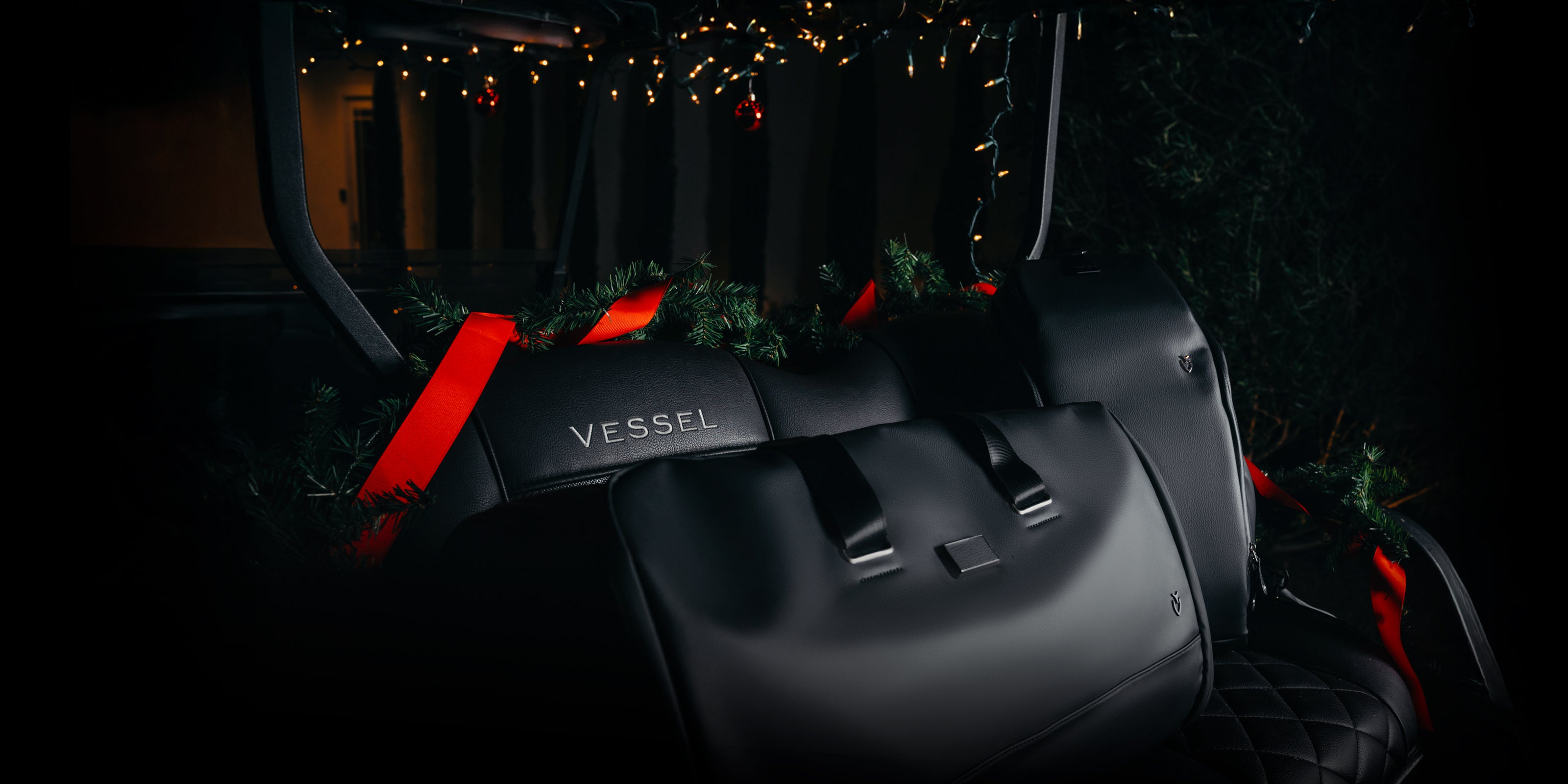 Black leather VESSEL Duffel sitting in a black golf cart, Christmas decorations