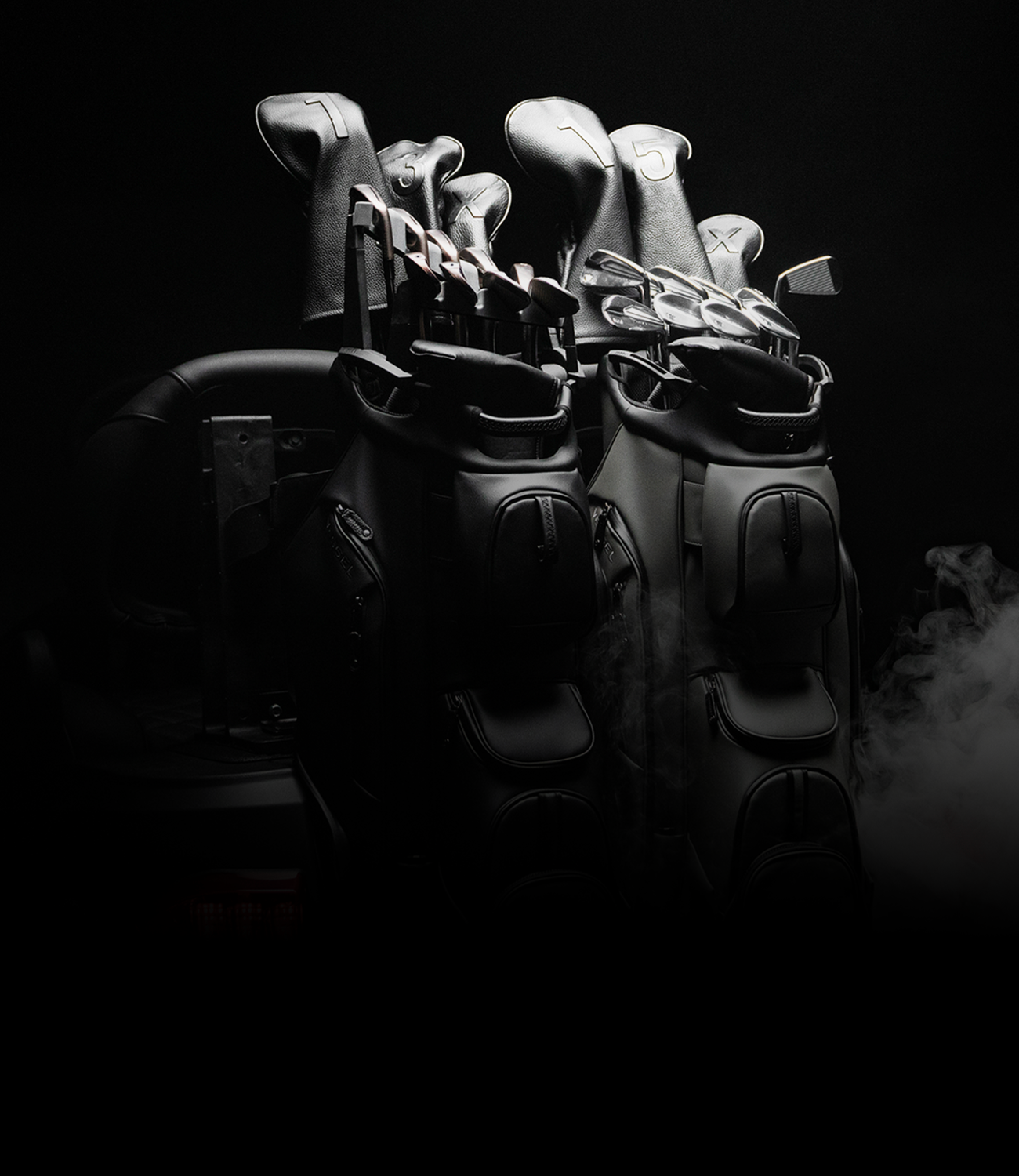Two leather golf cart bags sit on a golf cart, one is black, the other is grey.