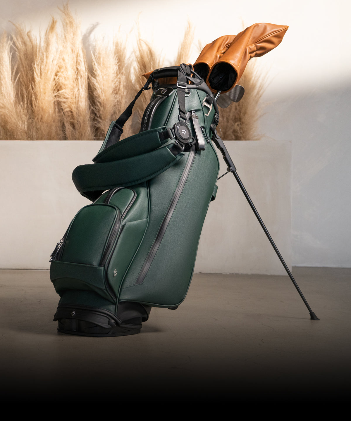 Green golf stand bag with brown leather club covers stands in a beige room, creating a stylish contrast.