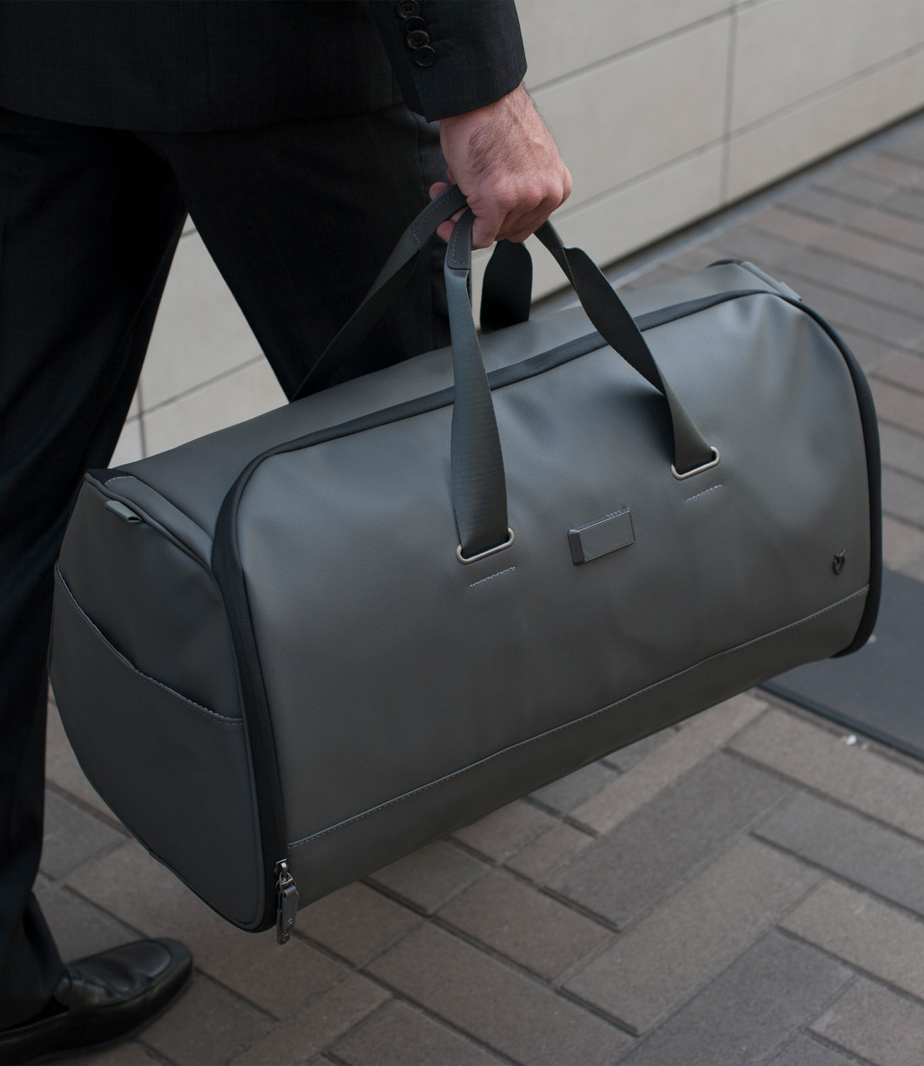 Close up of man carrying gray leather duffel bag
