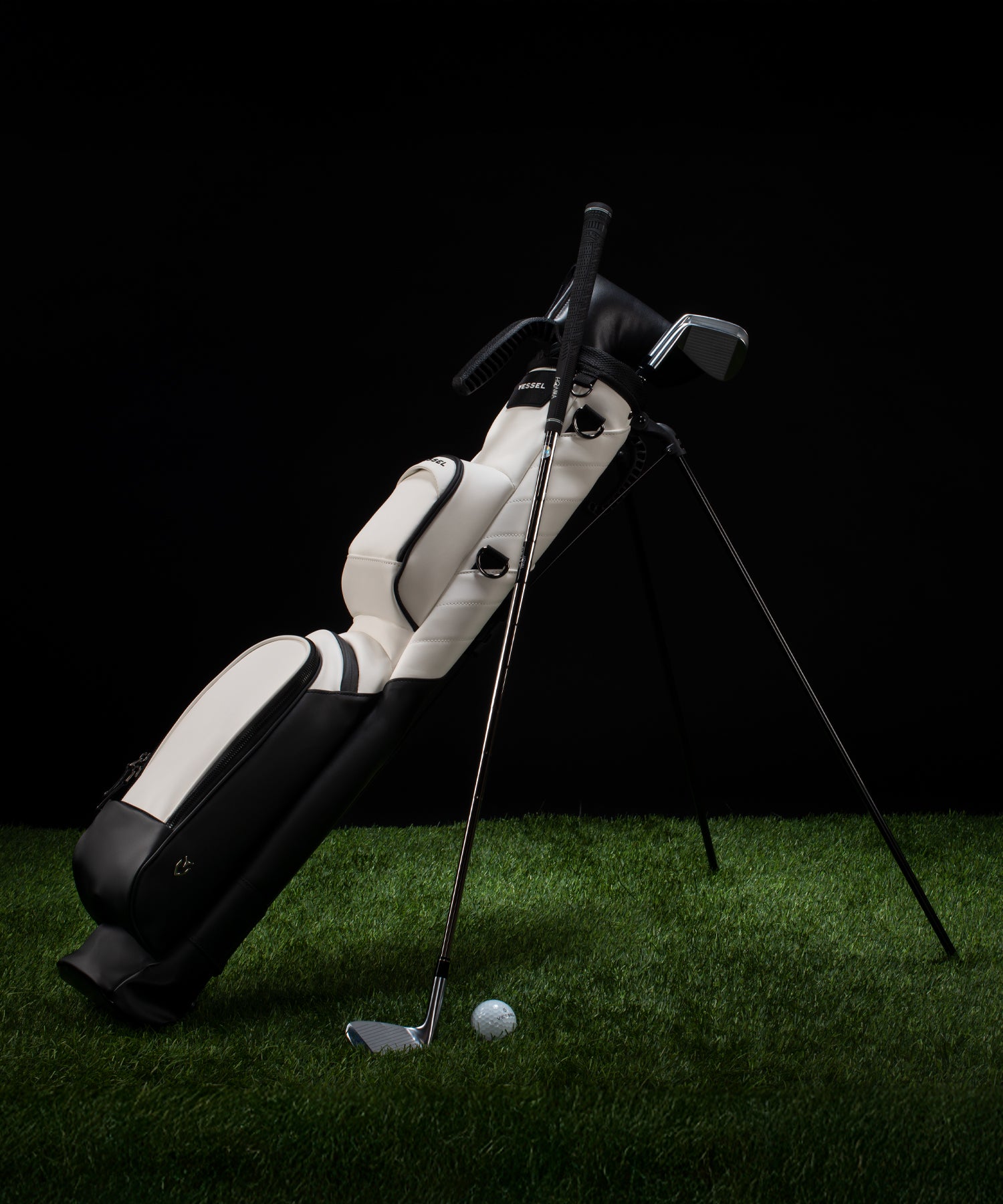 Black and white golf pencil stand bag on green grass with a golf club leaning against it