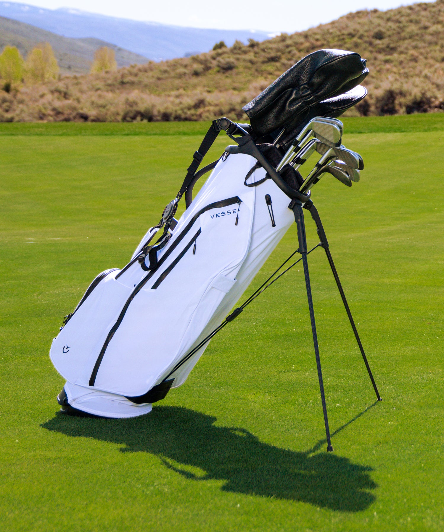 White lightweight golf bag full of golf clubs and golf club headcovers on a green golf course