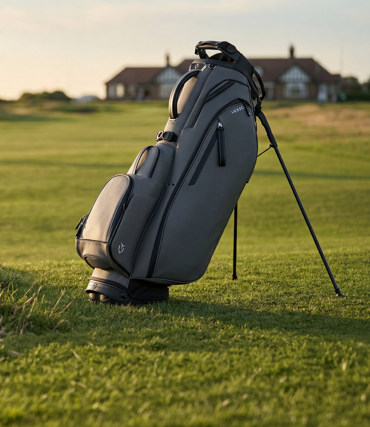 Grey leather golf bag on a green golf course with house in background