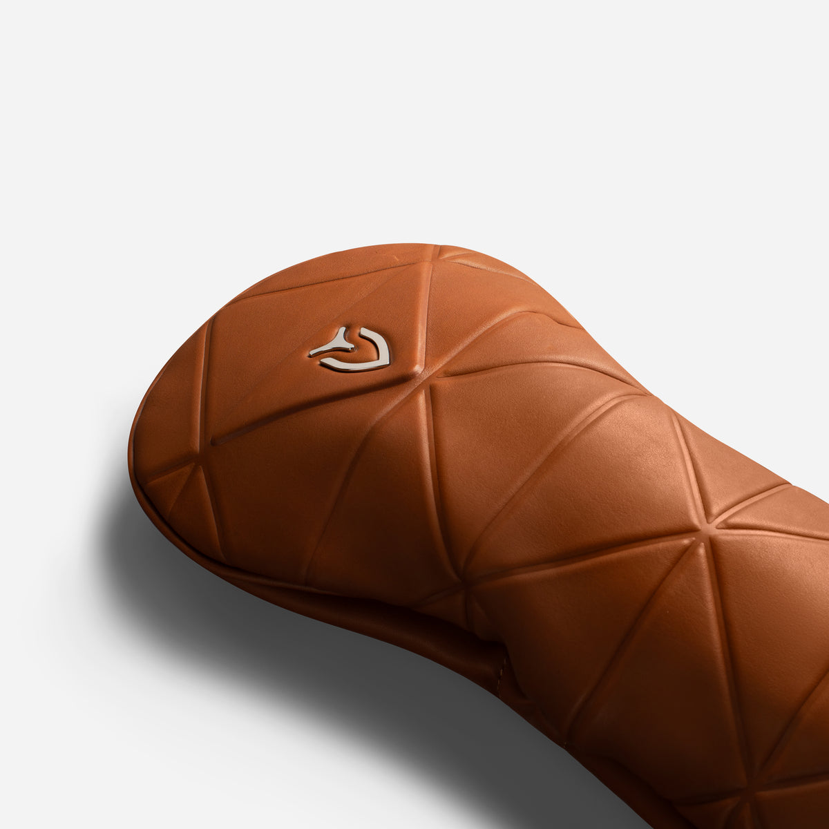 Close up of metal logo on brown geometric headcover on a white background