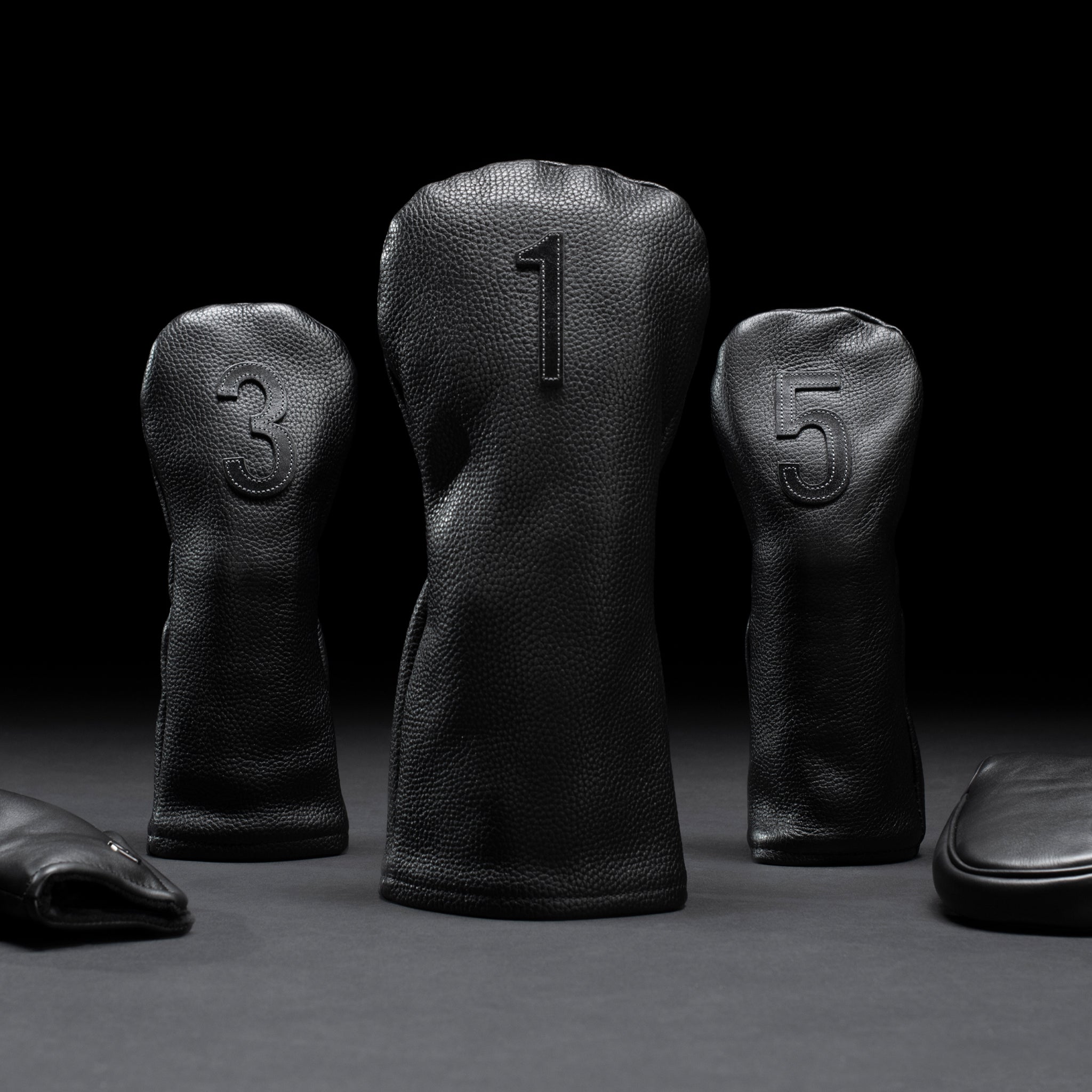 Three black golf headcovers propped up in black studio