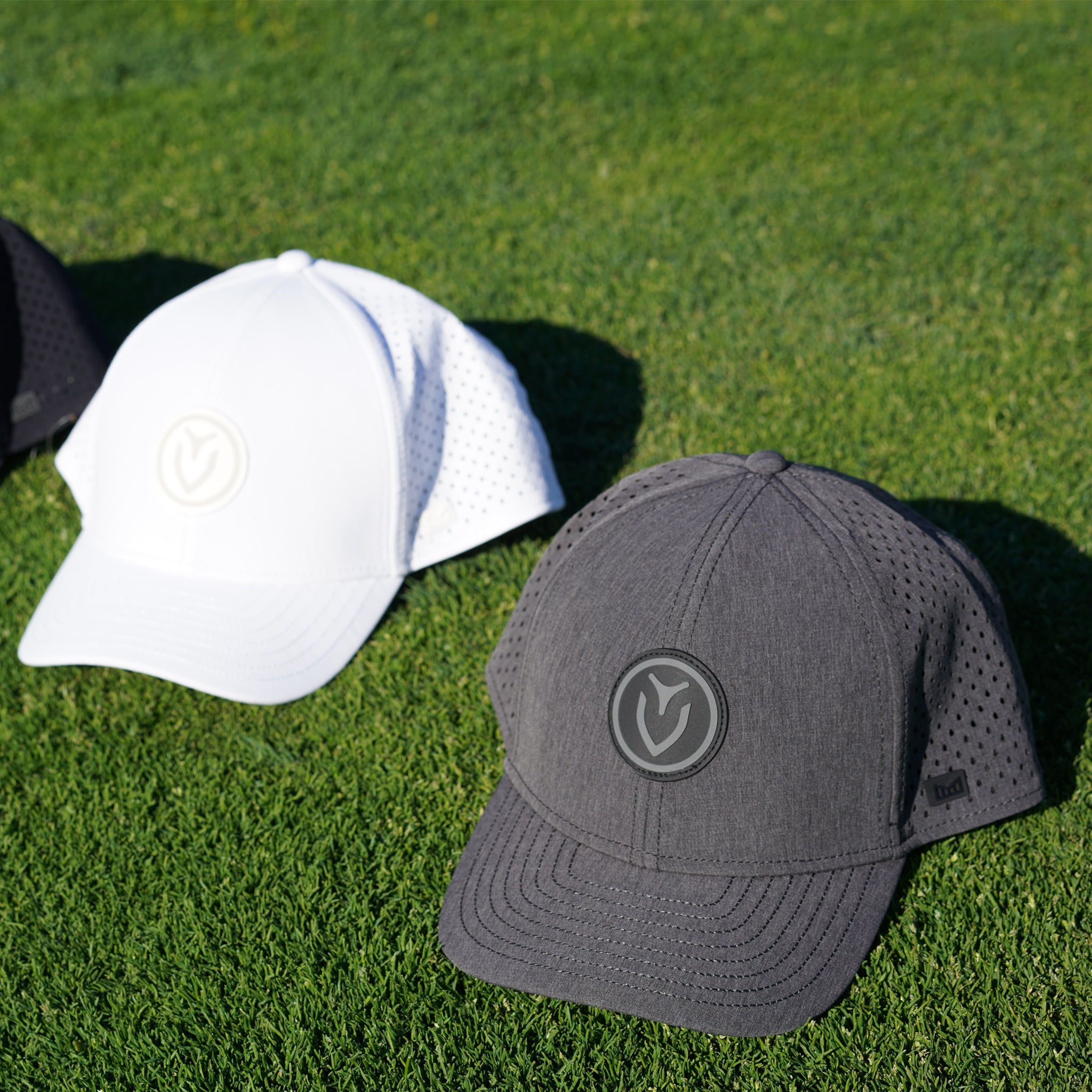 Three hats in different colors, black, white, and gray, next to each other on the grass