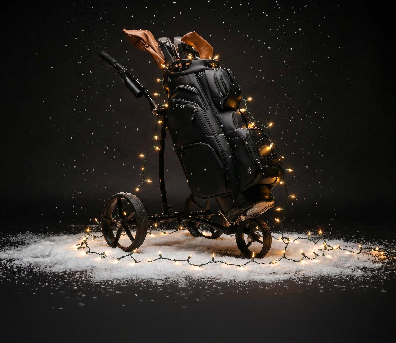 Black cart bag on push cart covered in Christmas lights on snowy background